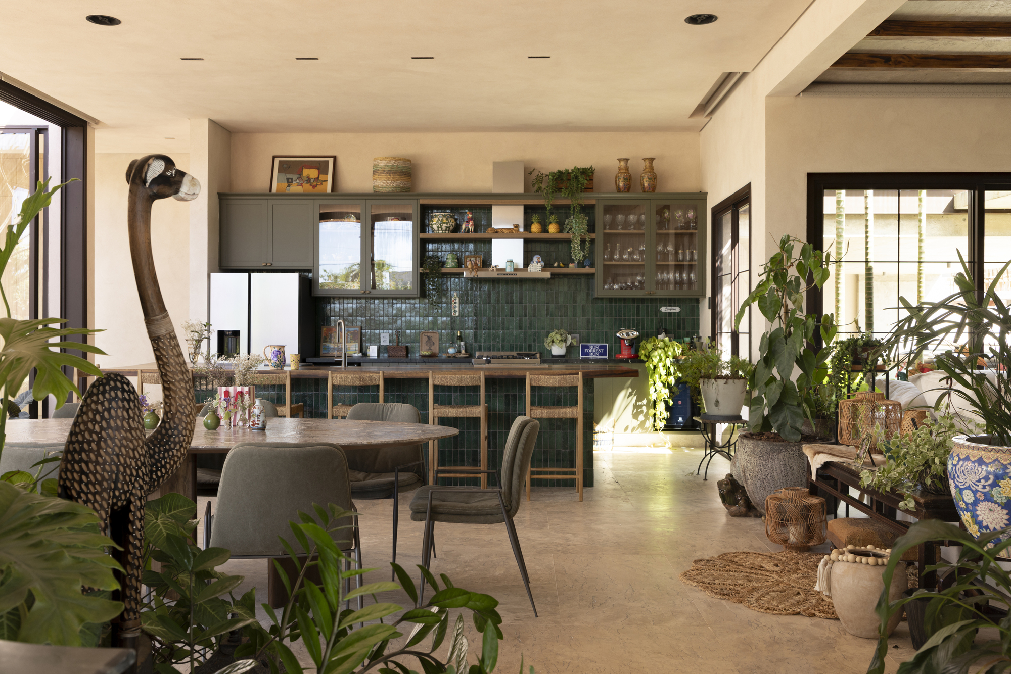 Open-plan kitchen and dining area with green tile backsplash, potted plants, and exposed timber ceiling beams