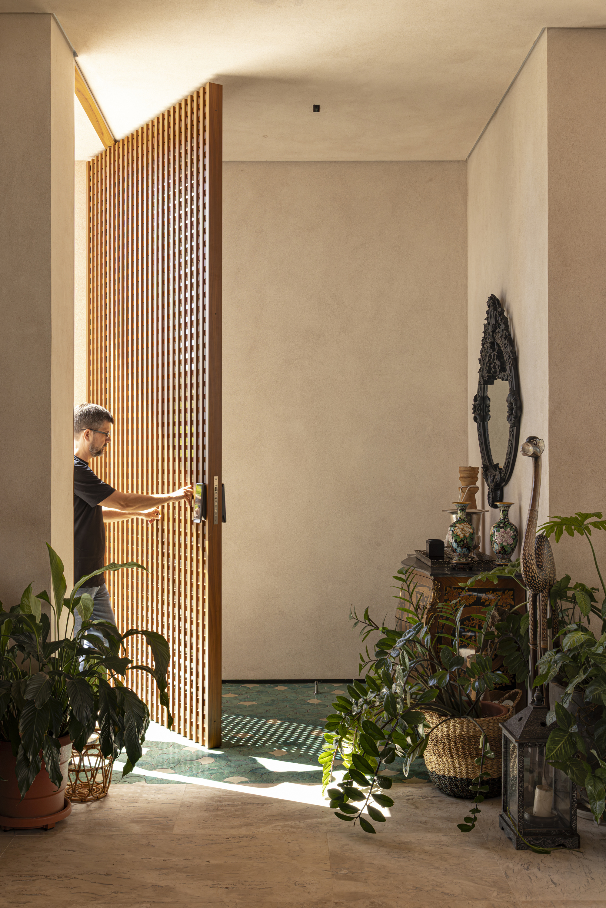 Entry foyer with curved vertical timber slat screen and person visible through the doorway beside potted plants