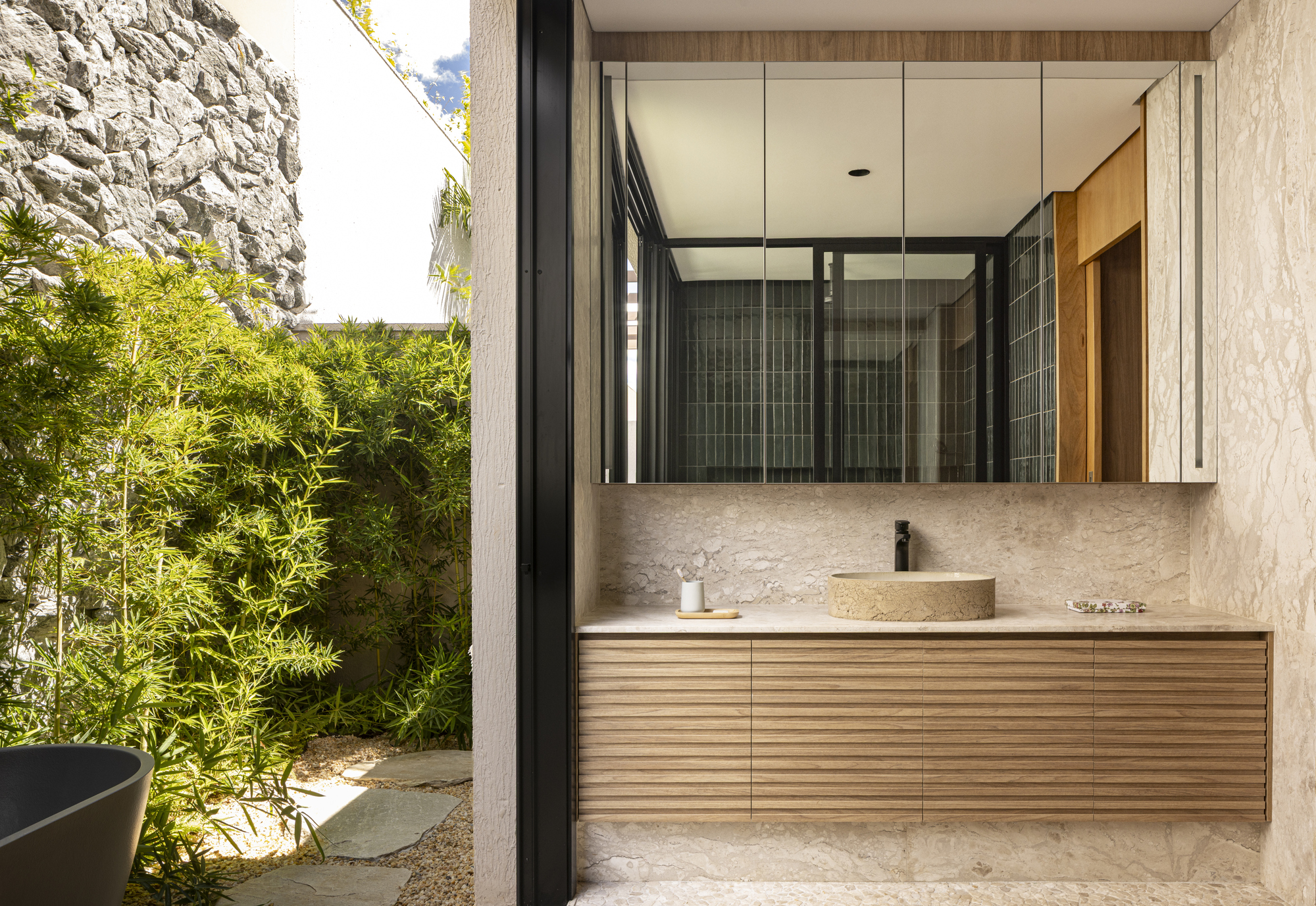 Bathroom vanity with stone countertop and timber cabinetry opening to bamboo courtyard