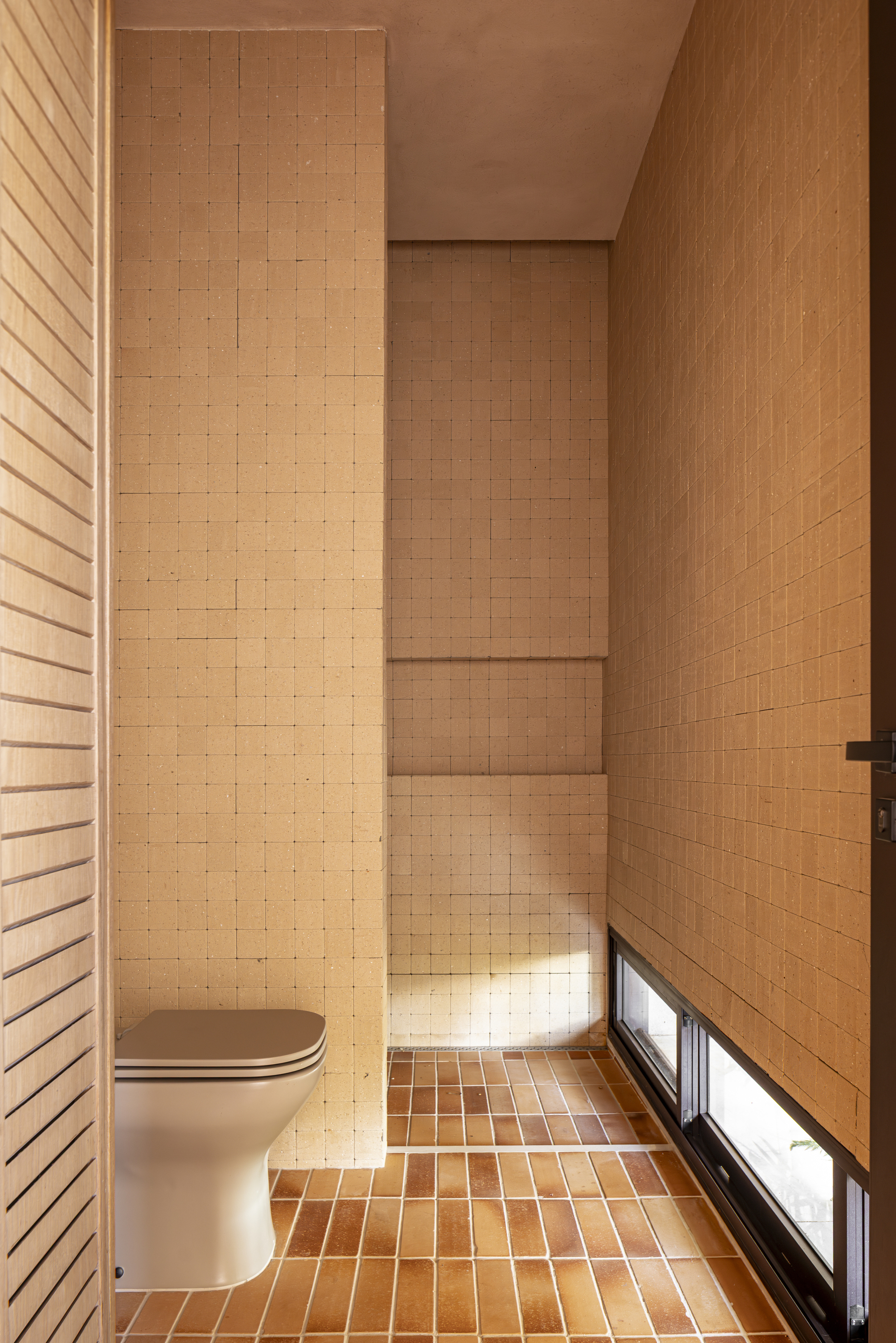 Tiled bathroom with timber wall panels and horizontal slit window at floor level