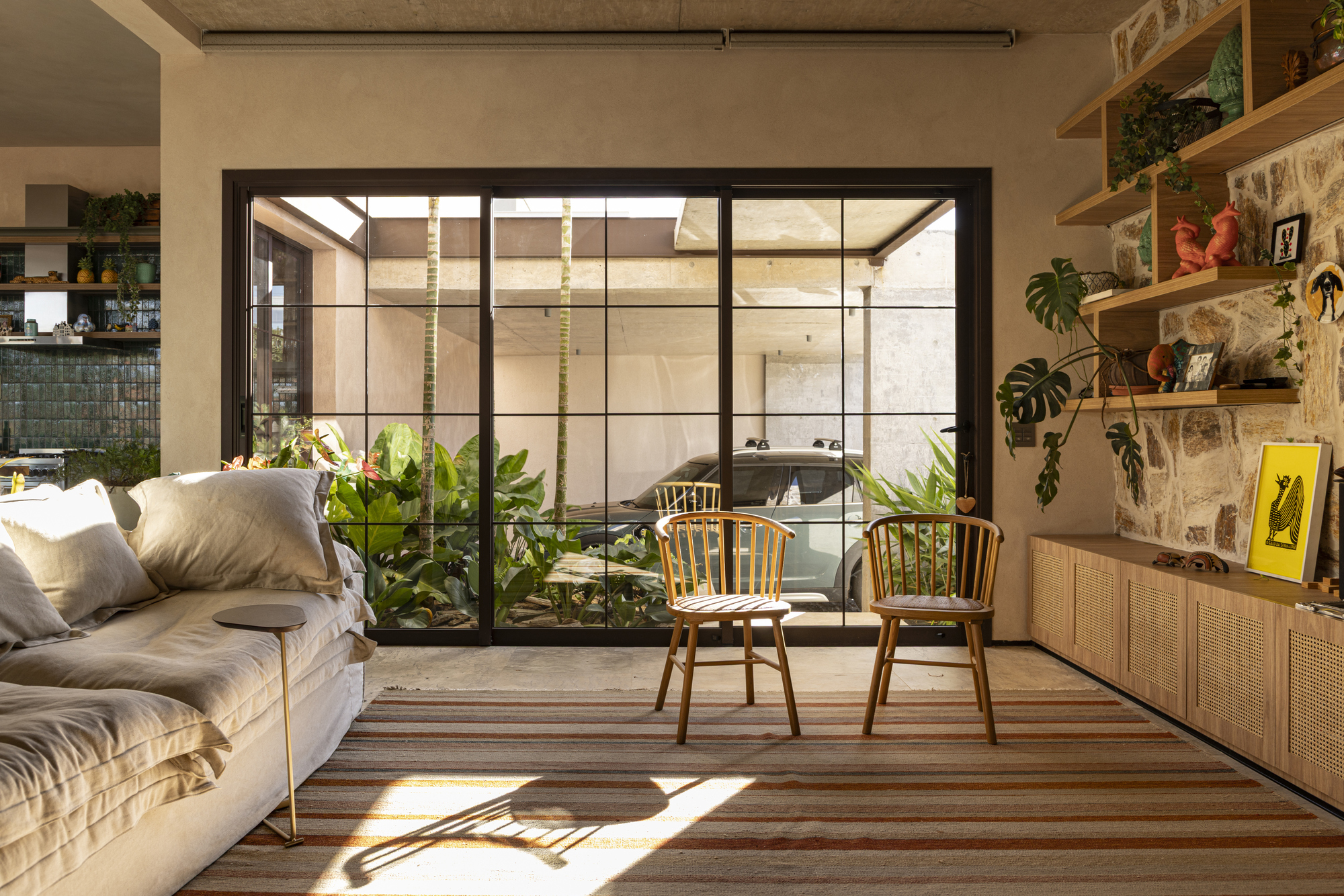 Steel-framed glazed wall separating the living area from a planted internal courtyard with spiral stair