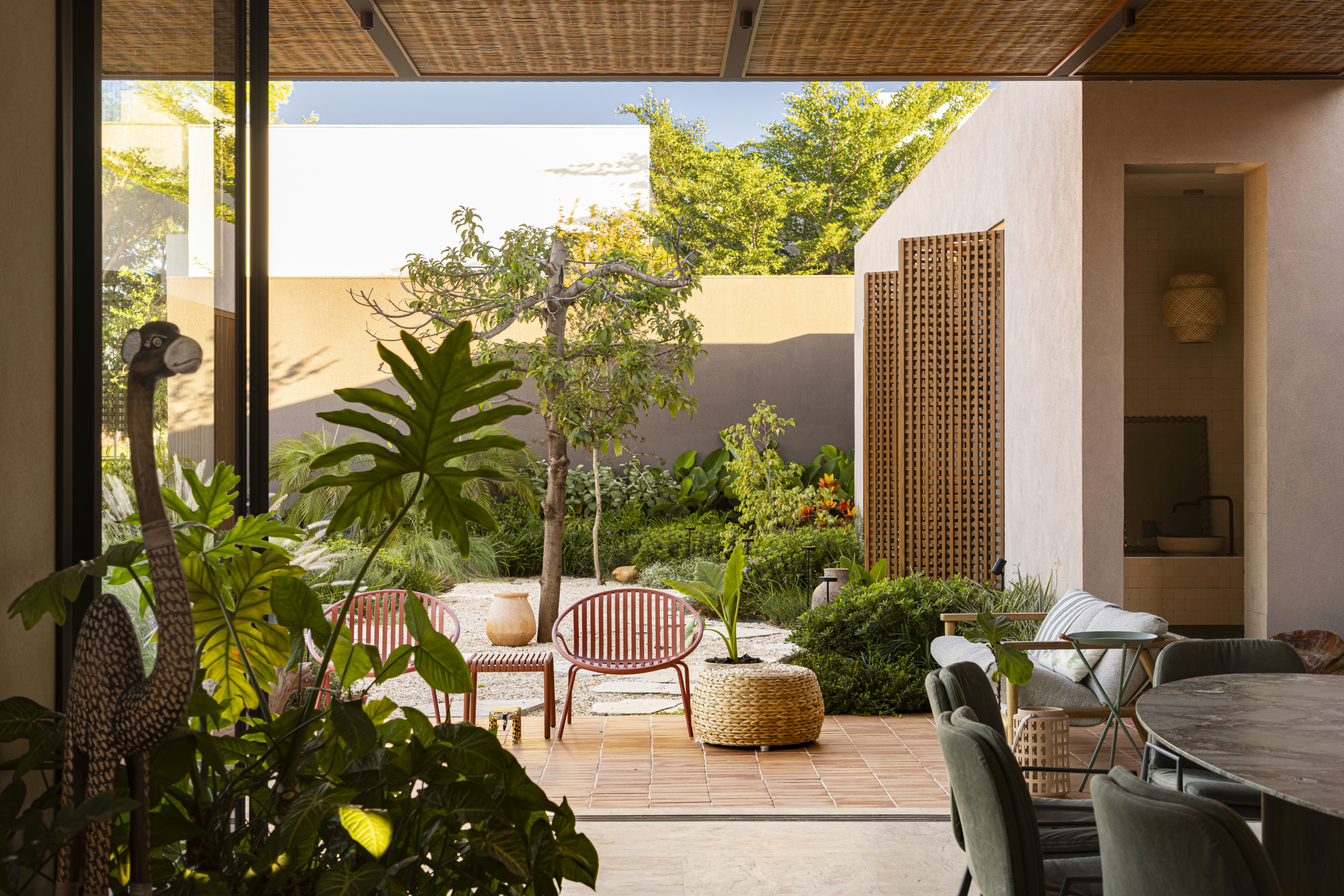 View from living space through woven ceiling to a planted courtyard with tile pavers and timber screens