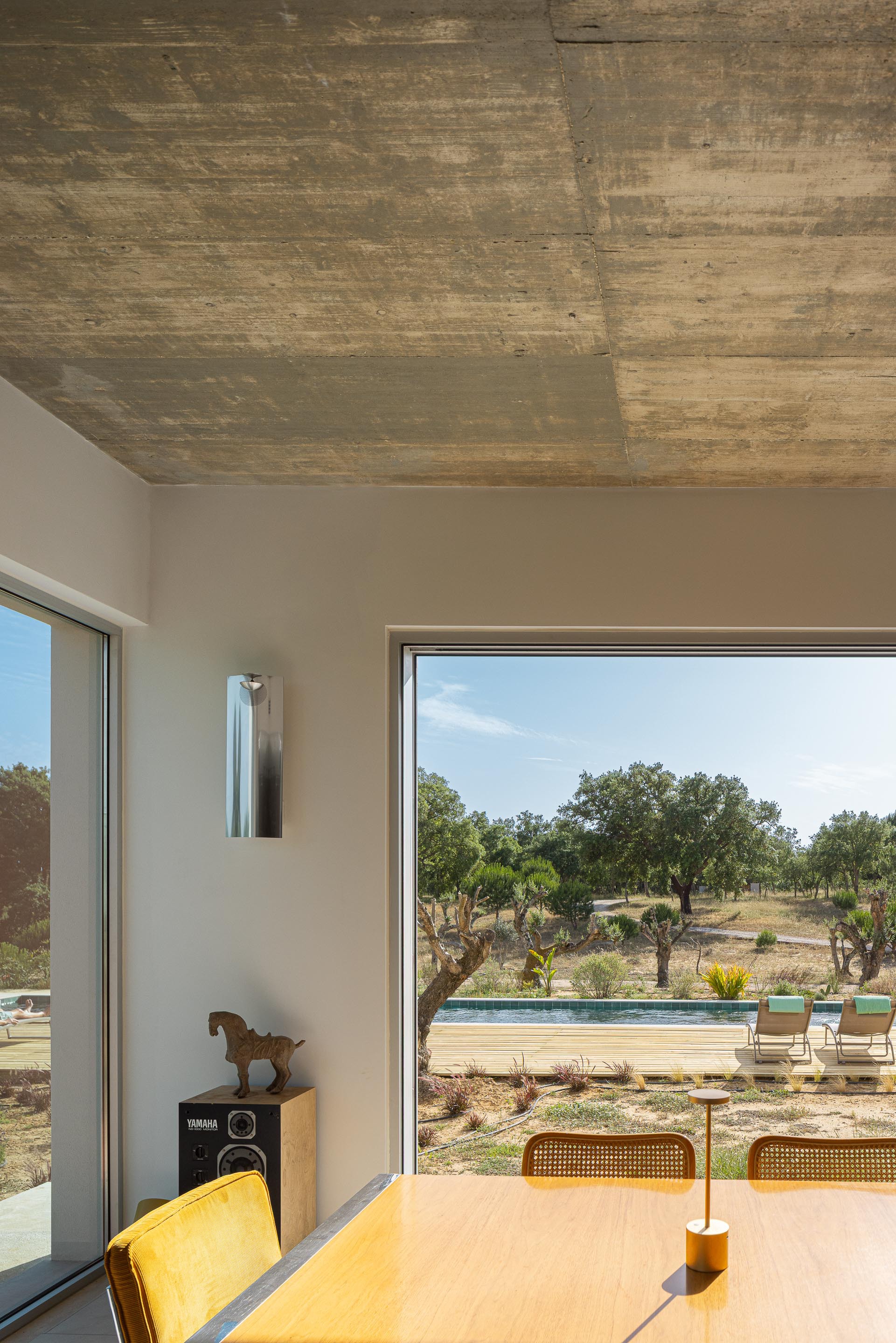Interior view through corner glazing to pool terrace with board-marked concrete ceiling above dining table