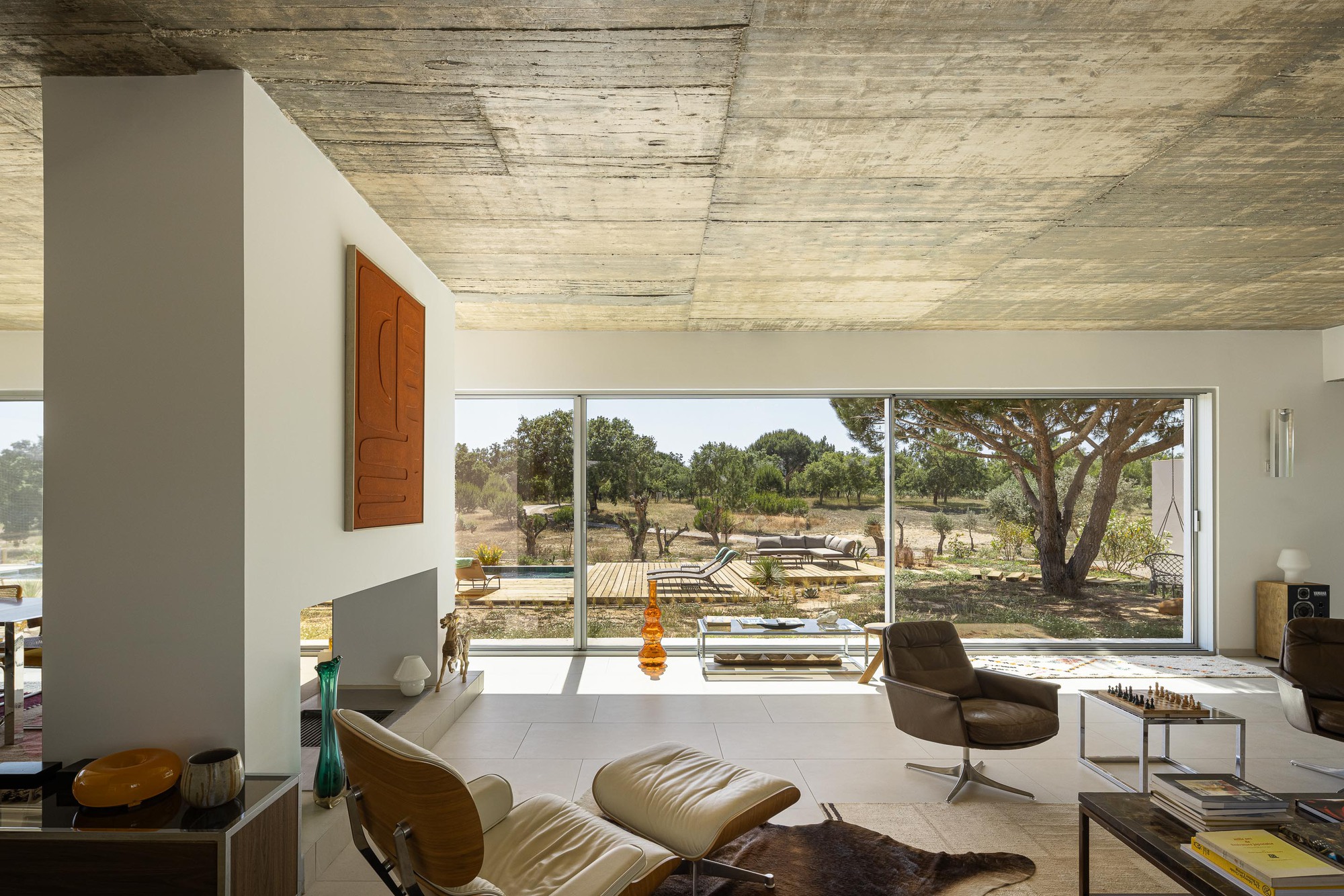 Living room with board-formed concrete ceiling and full-height glazing opening to a landscape of scattered trees