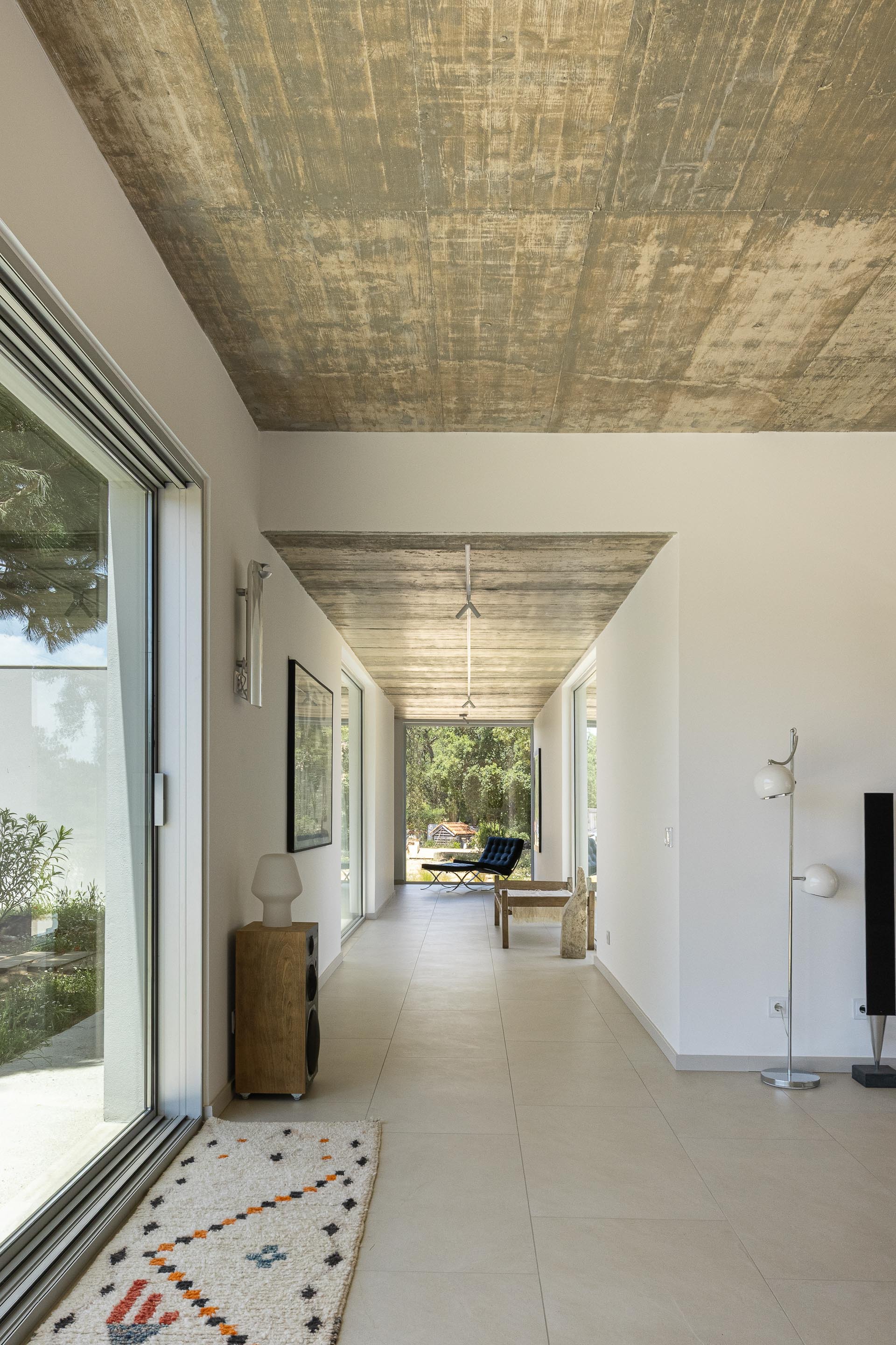 Long corridor with board-formed concrete ceiling and continuous glazing on both sides under bright daylight