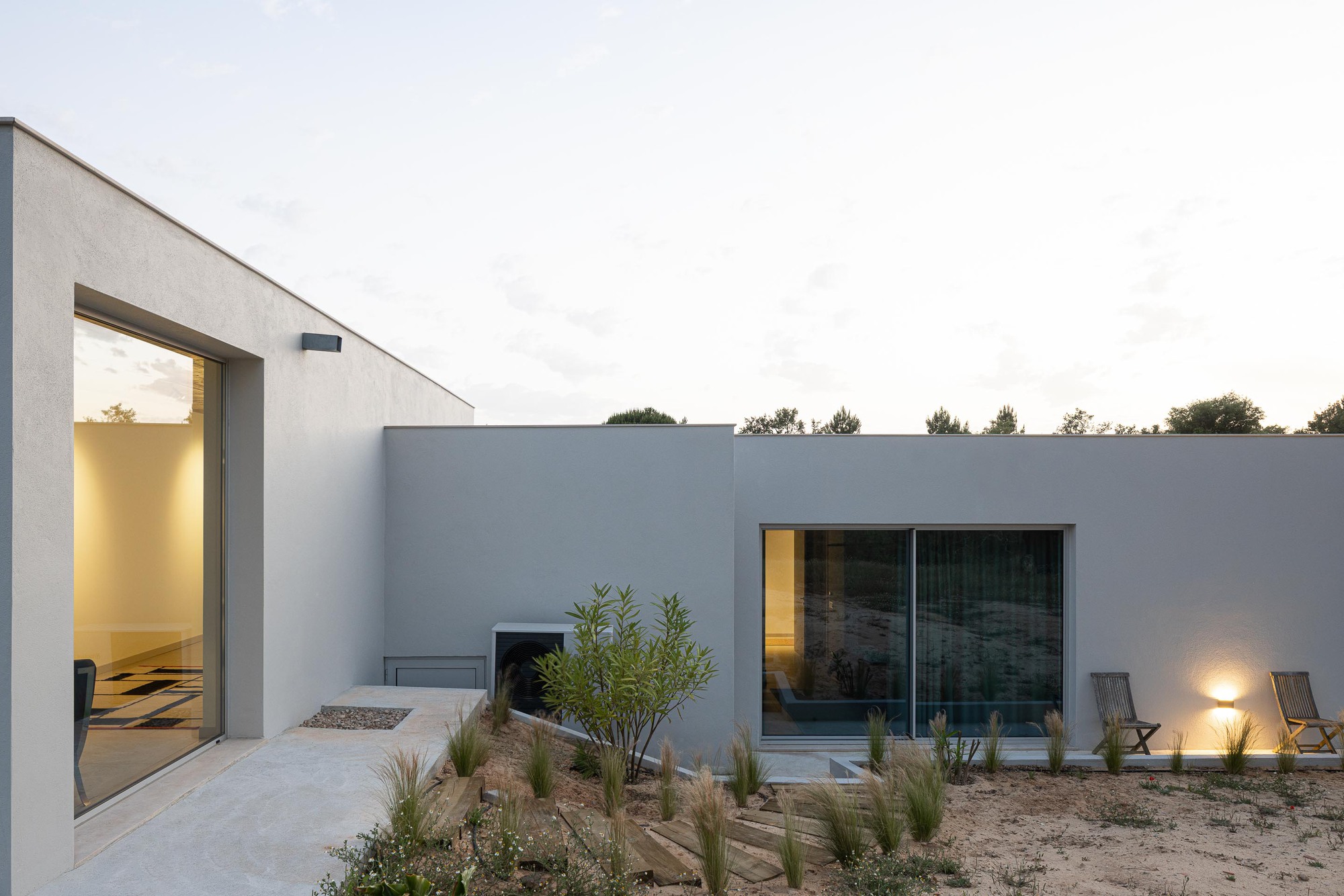 Private courtyard with planted beds, gravel paths, and two illuminated openings framing interior spaces at twilight