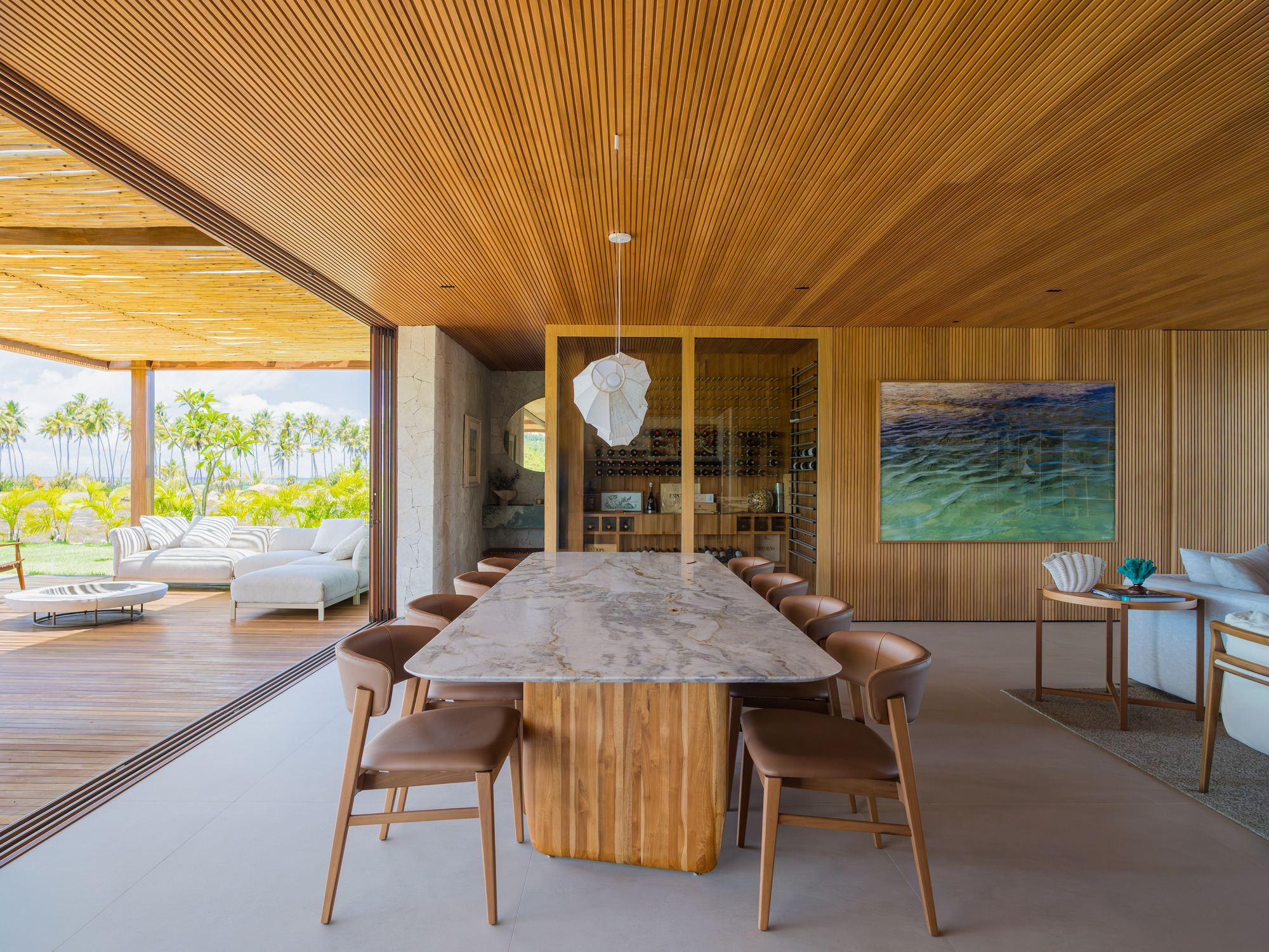 Dining room with timber-slatted ceiling, marble-topped table and floor-to-ceiling glazing opening to deck