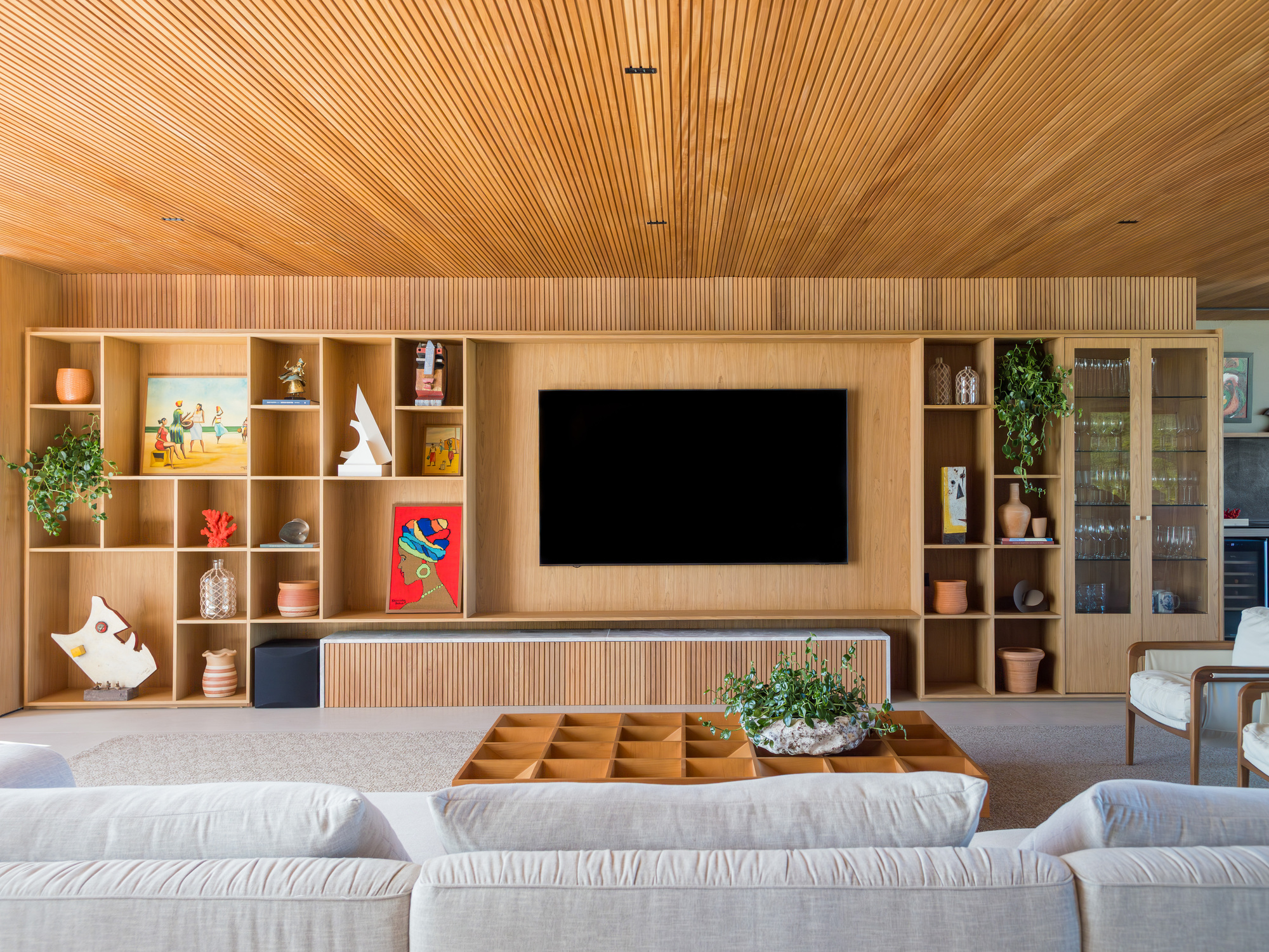 Living room with timber shelving wall, central media console and sectional seating under slatted ceiling