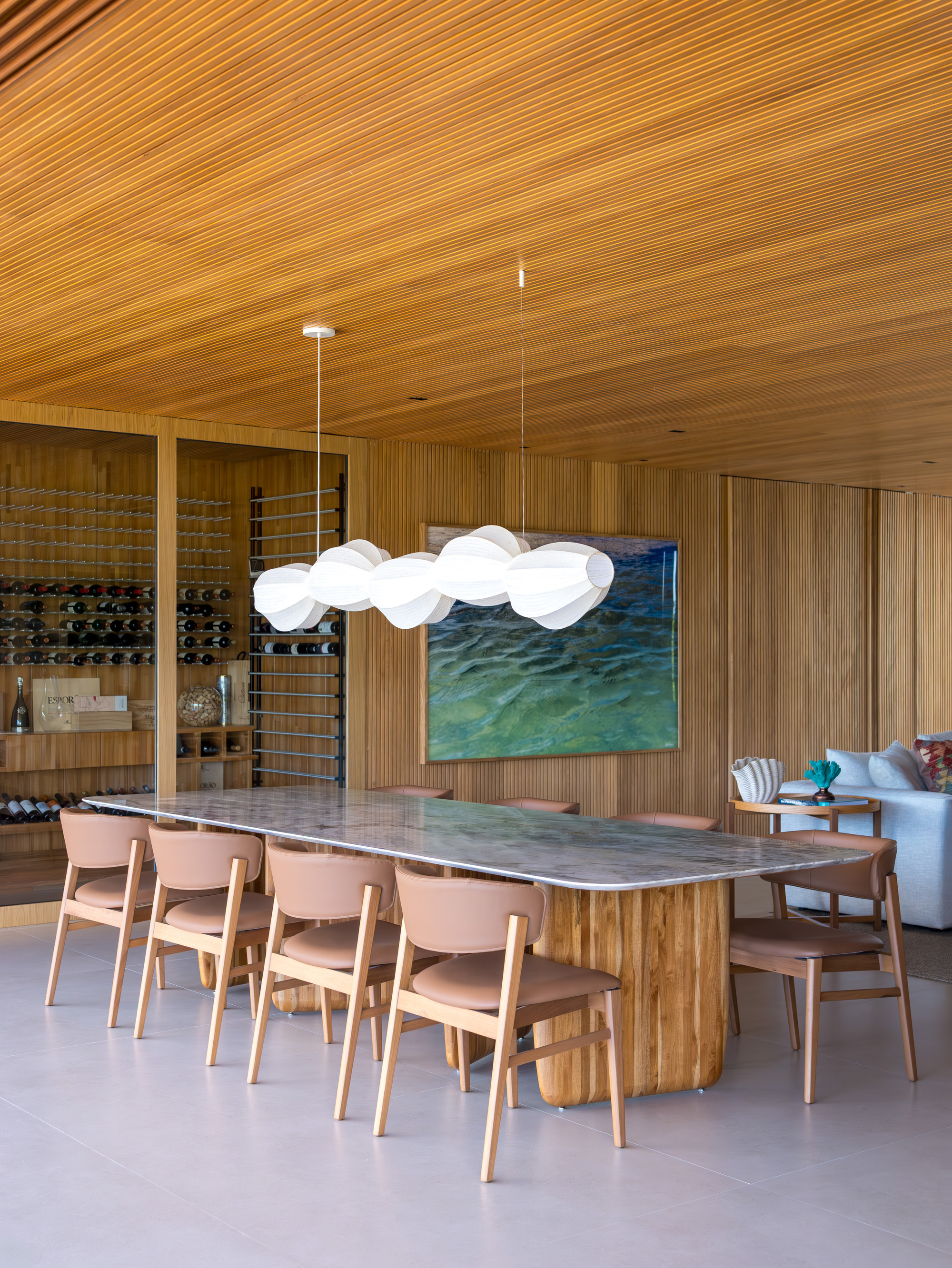 Dining room with slatted timber ceiling and walls surrounding a marble-top table with white pendant lighting