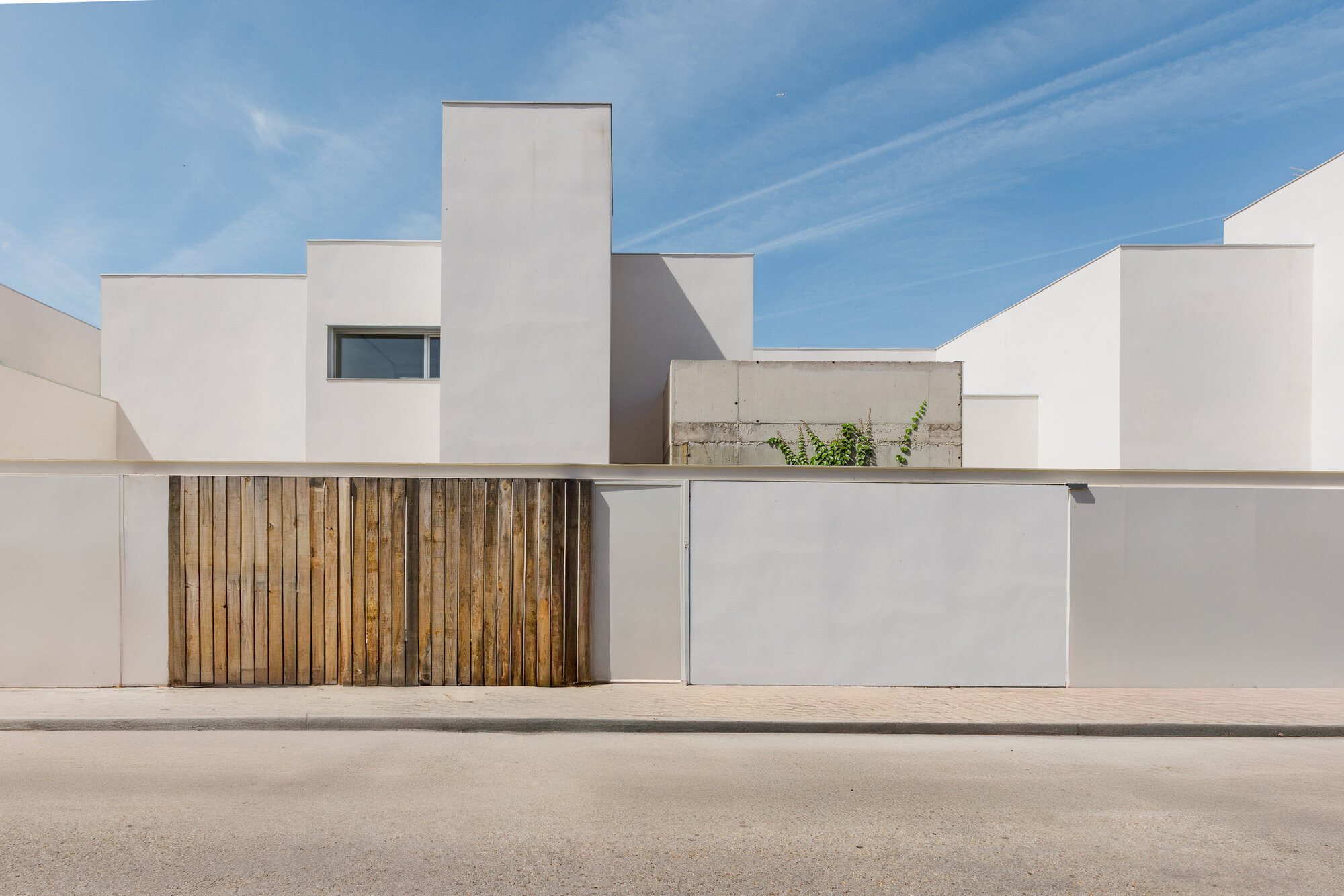 Street view of the white rendered facade with vertical timber gate panels under a clear sky