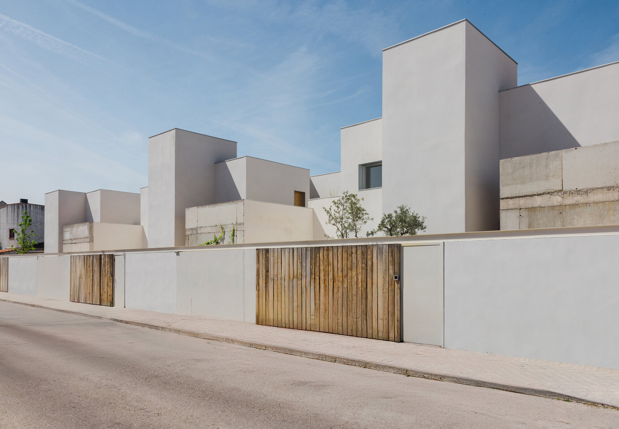 Street elevation showing staggered white volumes with timber gate sections and planted rooftop terraces