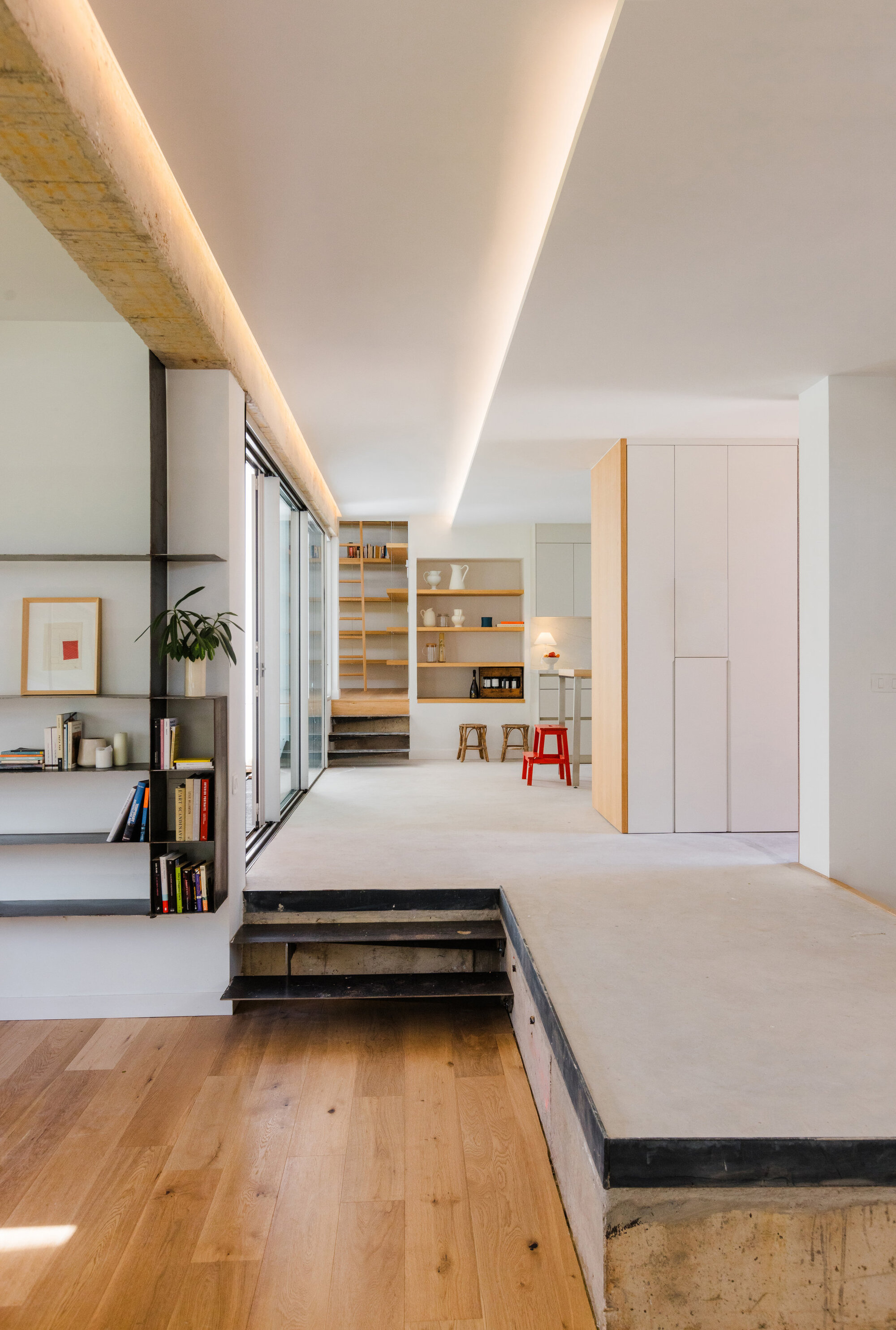 Open plan interior with recessed linear ceiling light, raised concrete platform and oak flooring