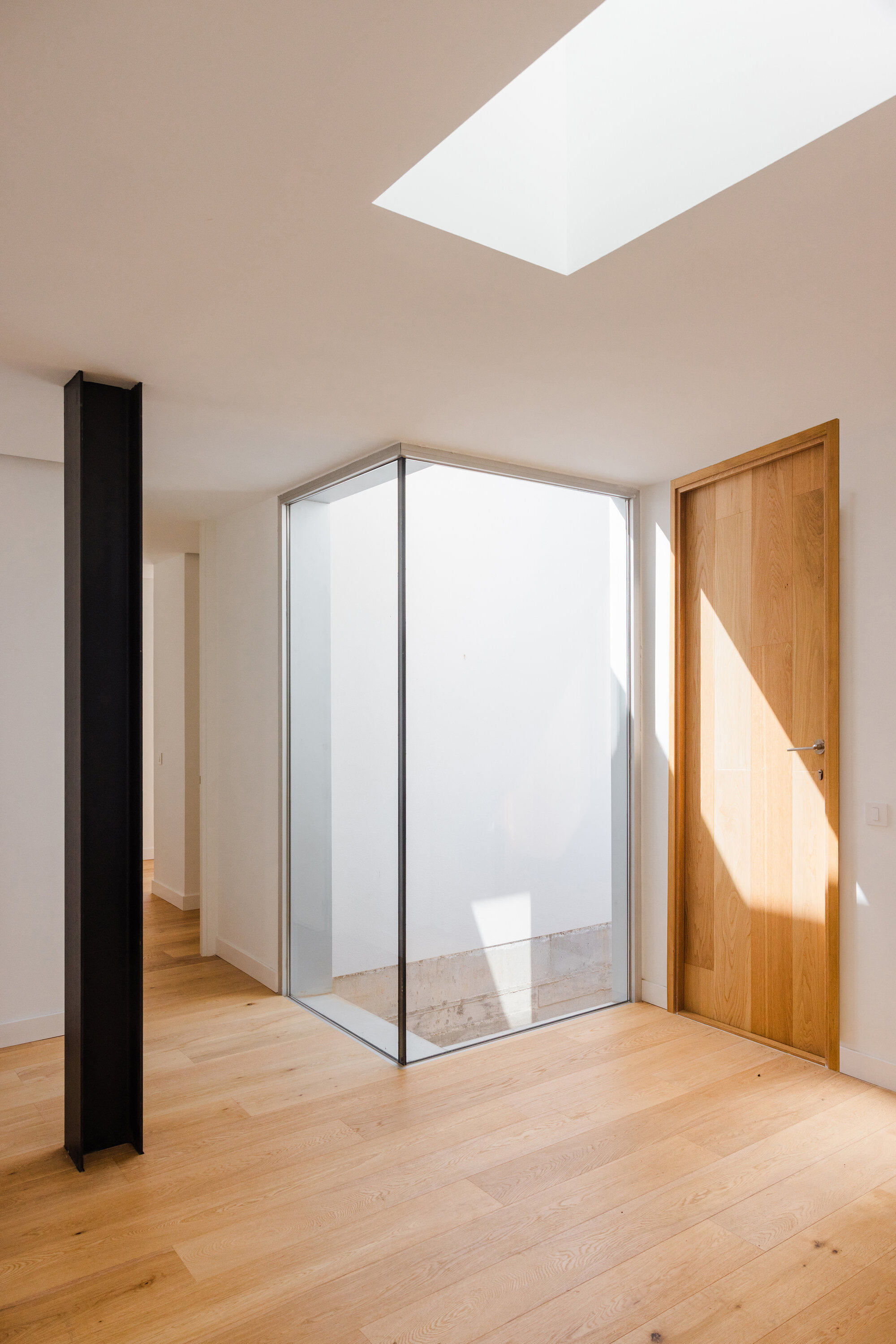 Interior corner with glass-walled courtyard, oak door and skylight casting afternoon shadows