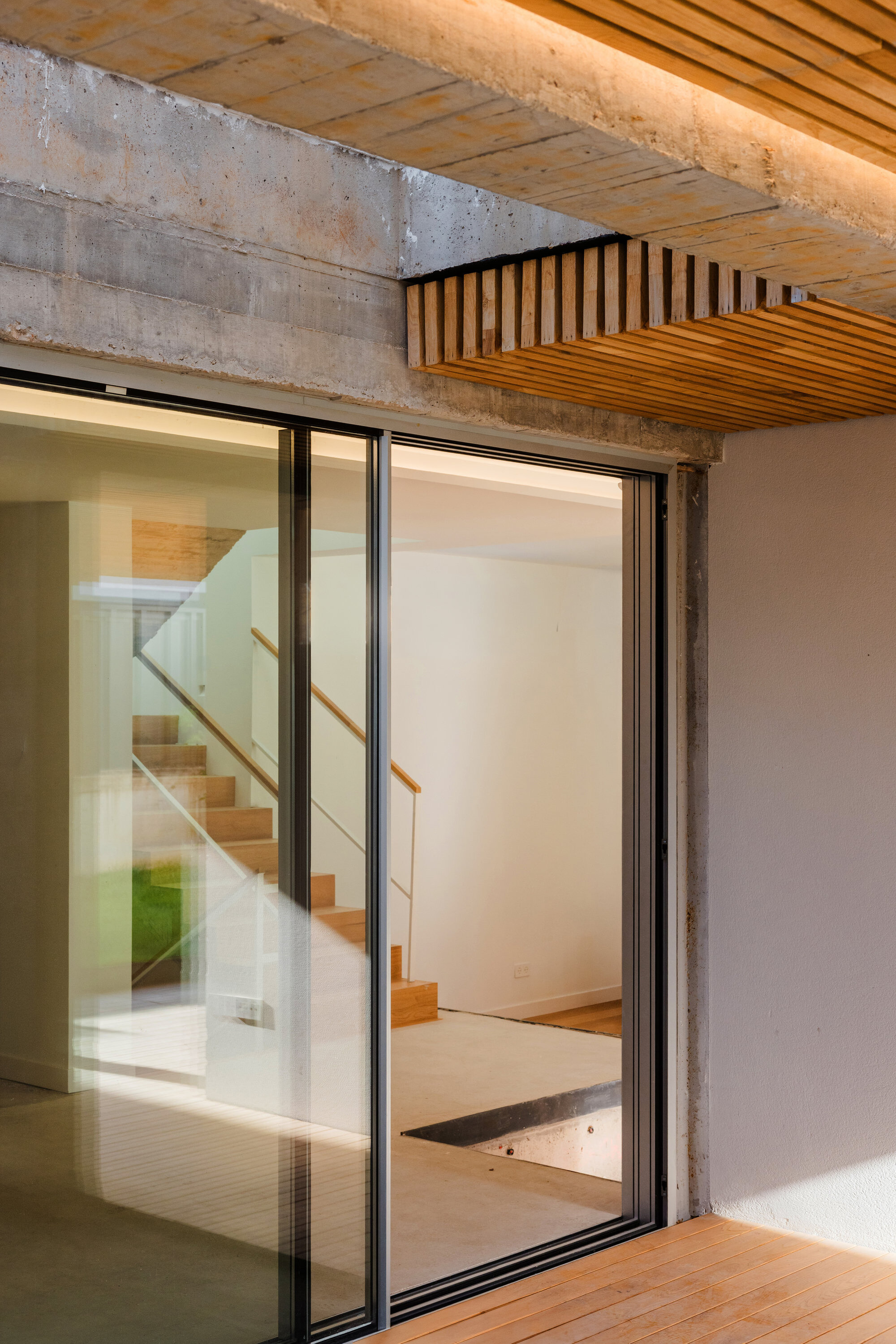 Exposed concrete beam with timber slat ceiling and open sliding glass door revealing internal staircase