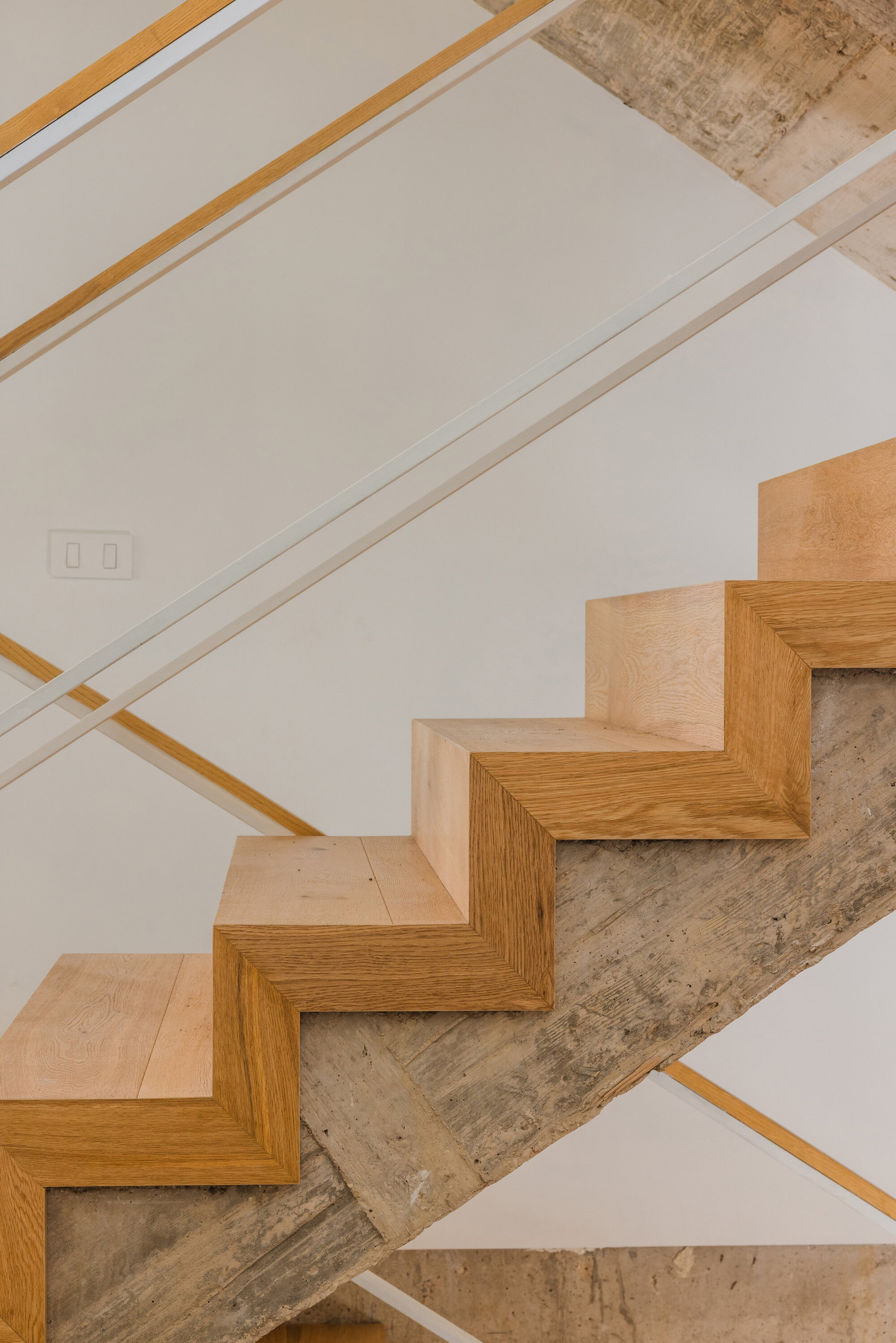 Angled view of oak stair treads turning around the raw concrete stair structure