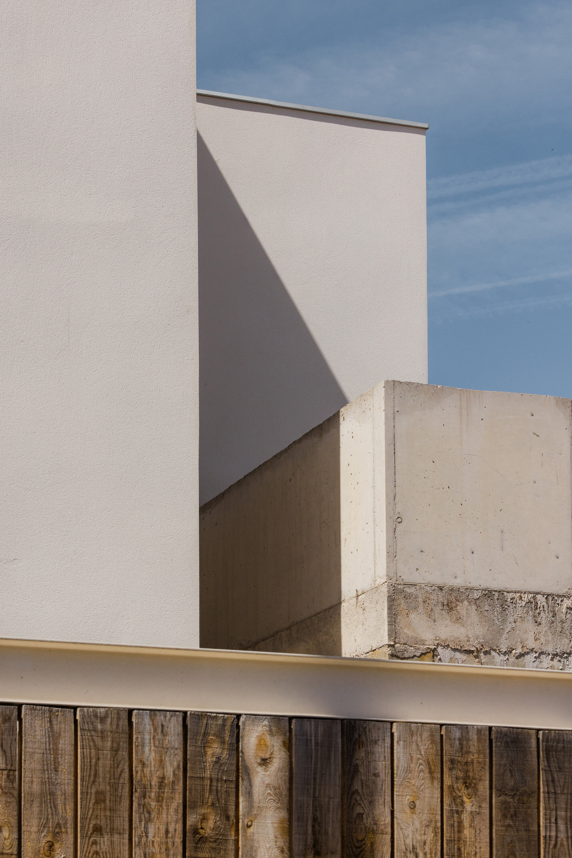 White stucco volumes meeting concrete pillar above vertical timber fence in afternoon sun