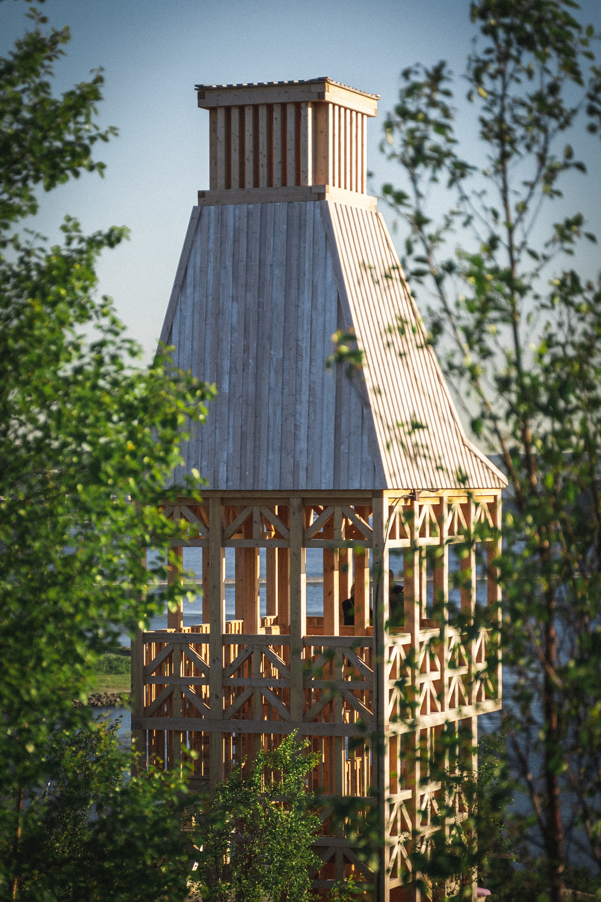 Lantern-topped wooden tower with lattice walls and vertical slat cladding framed by surrounding foliage