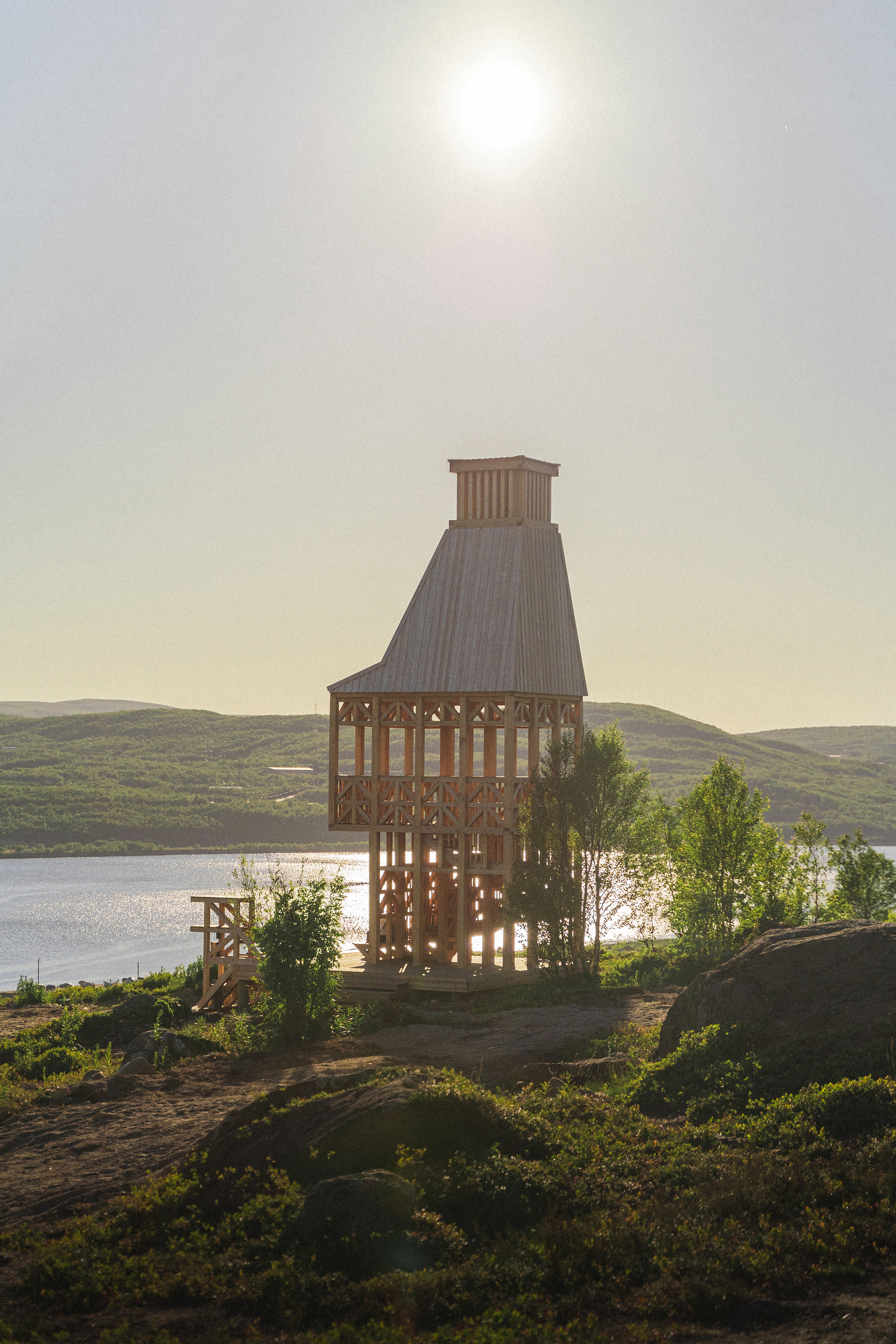 Backlit tower with open timber framework silhouetted against low sun over distant lake and hills