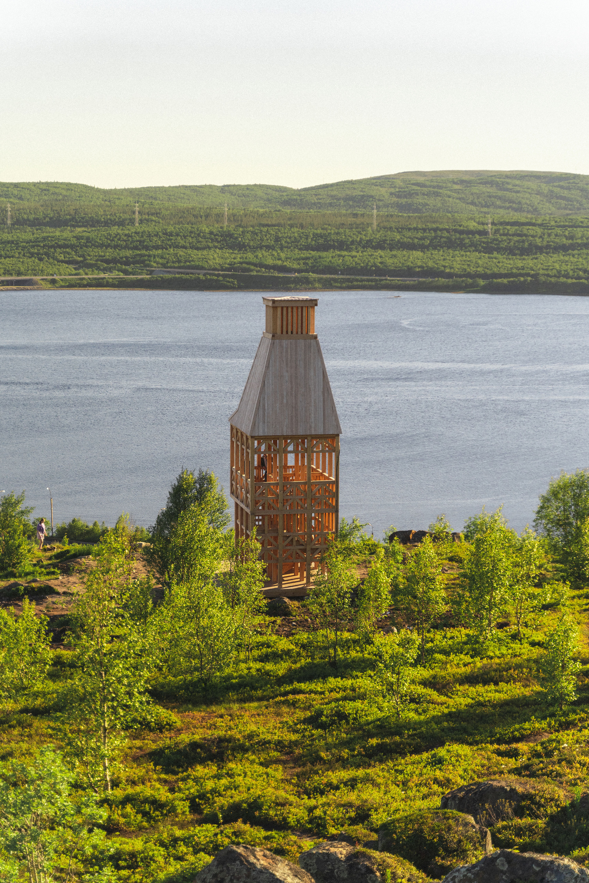 Timber lookout tower on vegetated slope overlooking calm lake and forested hillside in afternoon light