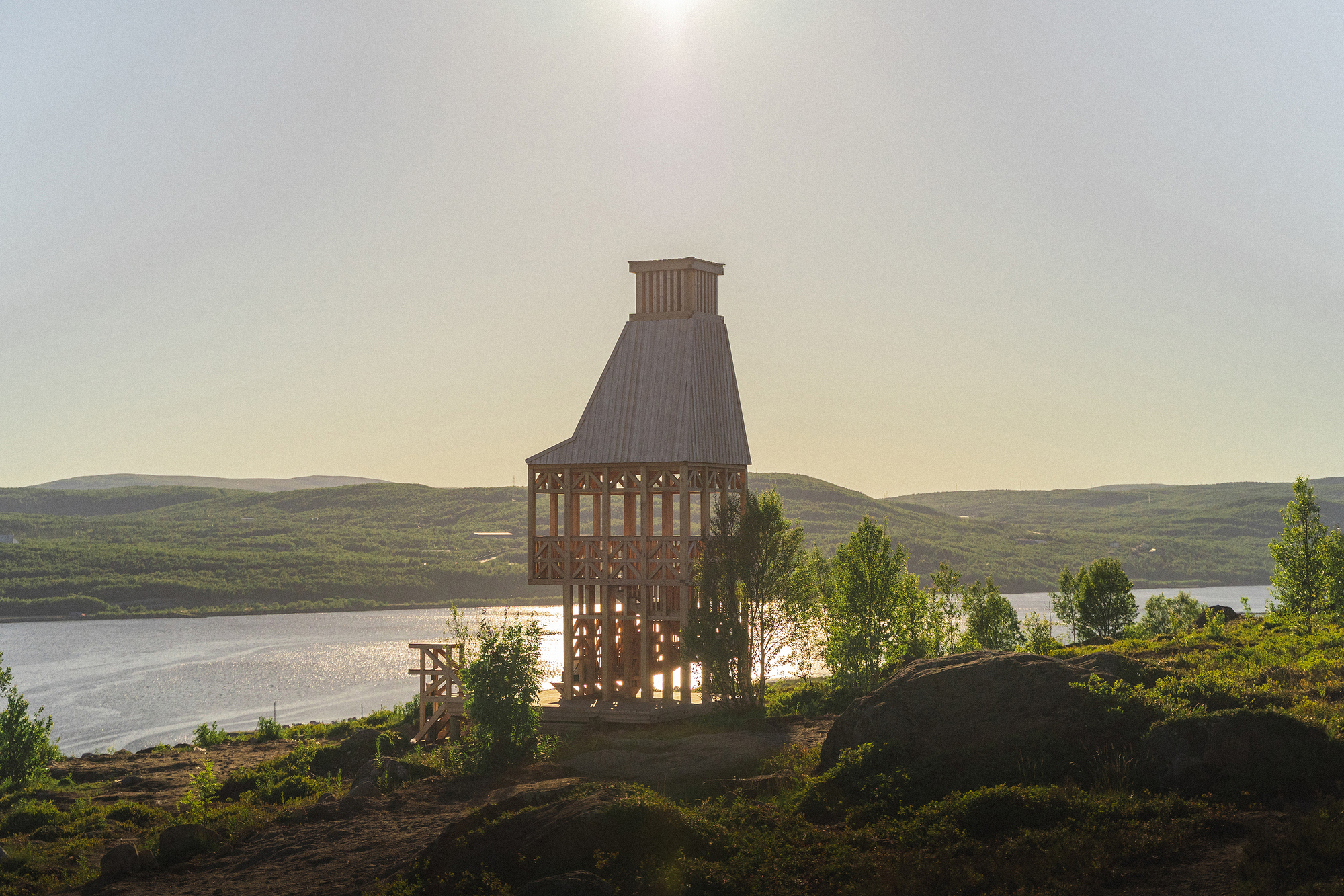 Timber frame tower with latticed walls silhouetted at sunset above a rocky coastal landscape