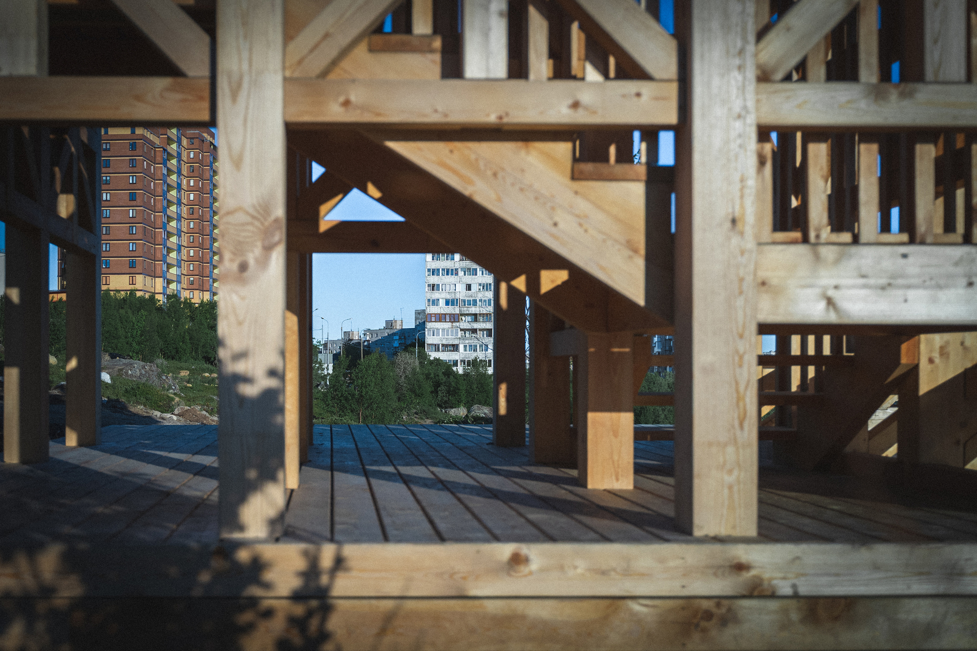 Interior view through exposed timber framing toward apartment buildings beyond the open structure