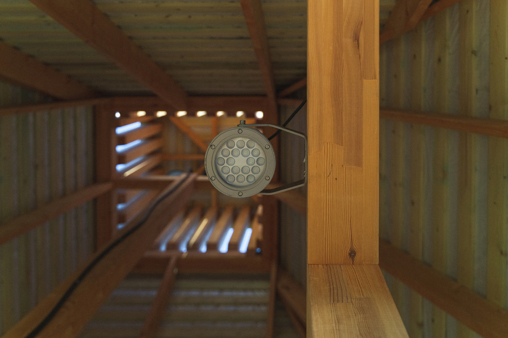 Looking up through the timber frame interior showing a mounted LED fixture and open rafters