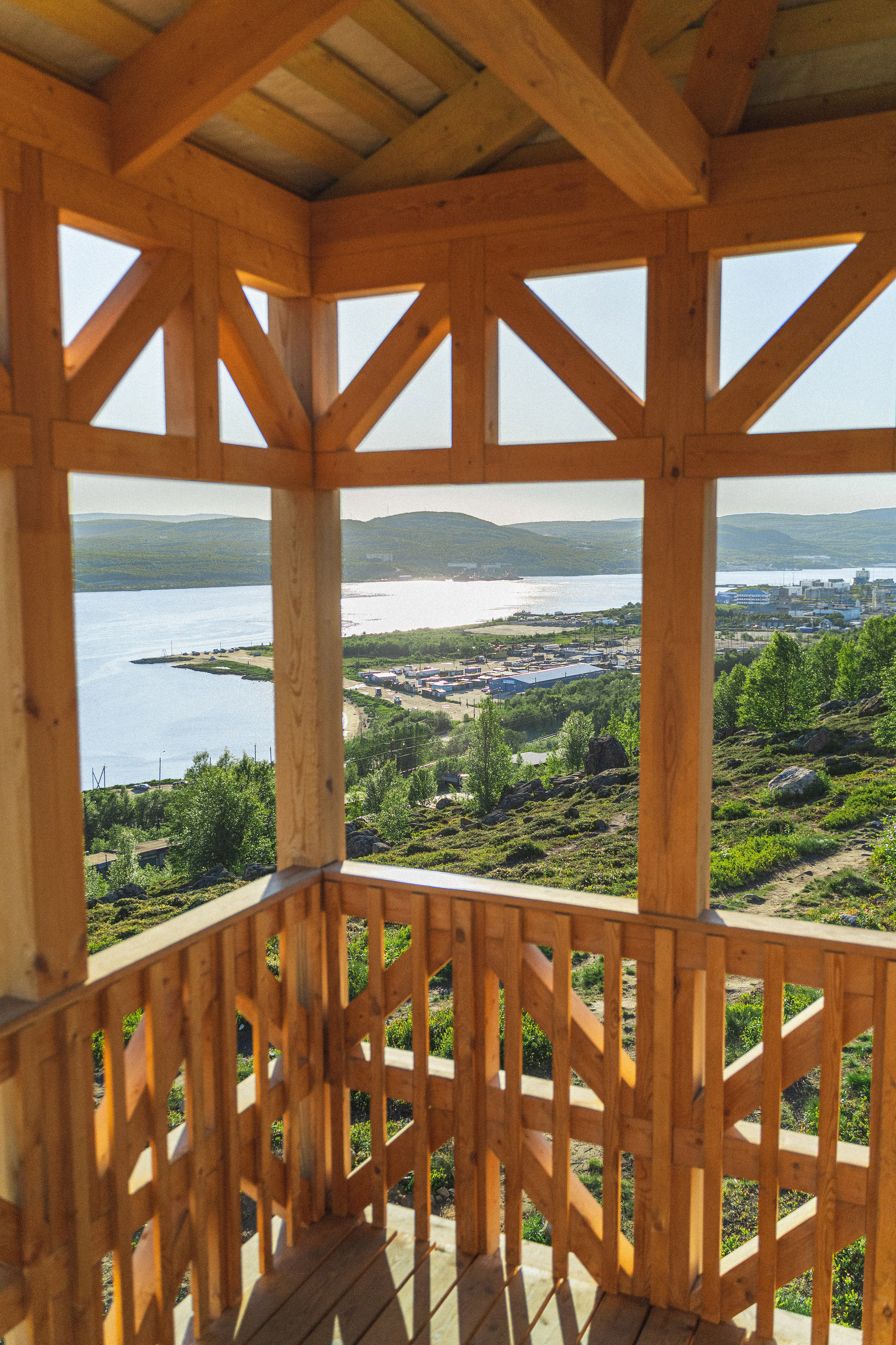 Timber belvedere with patterned screen railings overlooking a fjord and distant hills in summer
