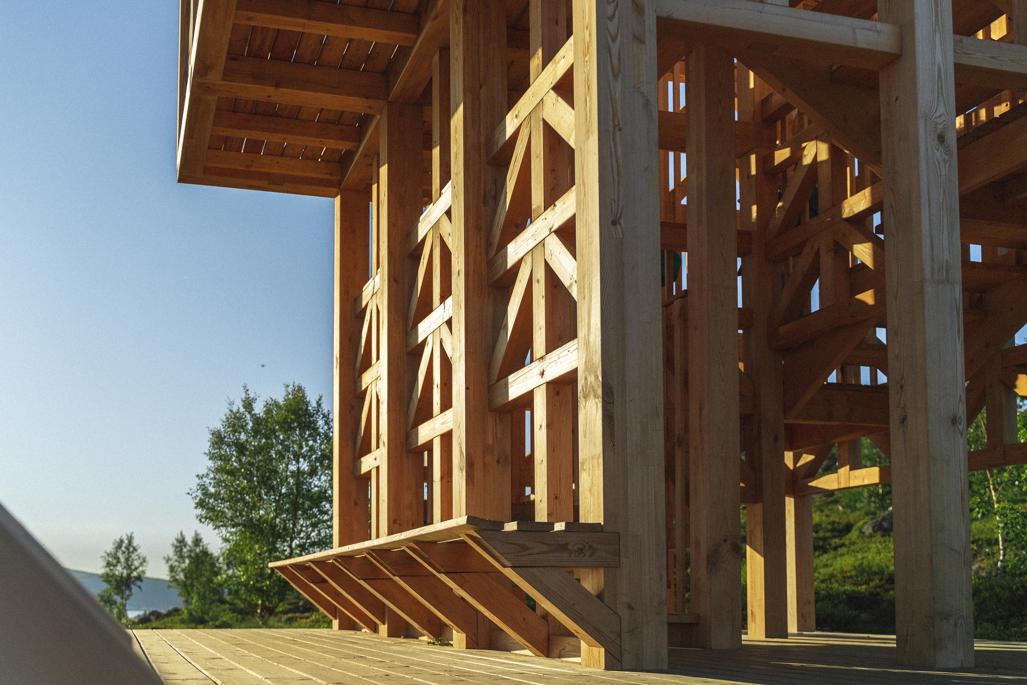 Angled view showing the cantilevered timber benches and structural columns under a clear blue sky