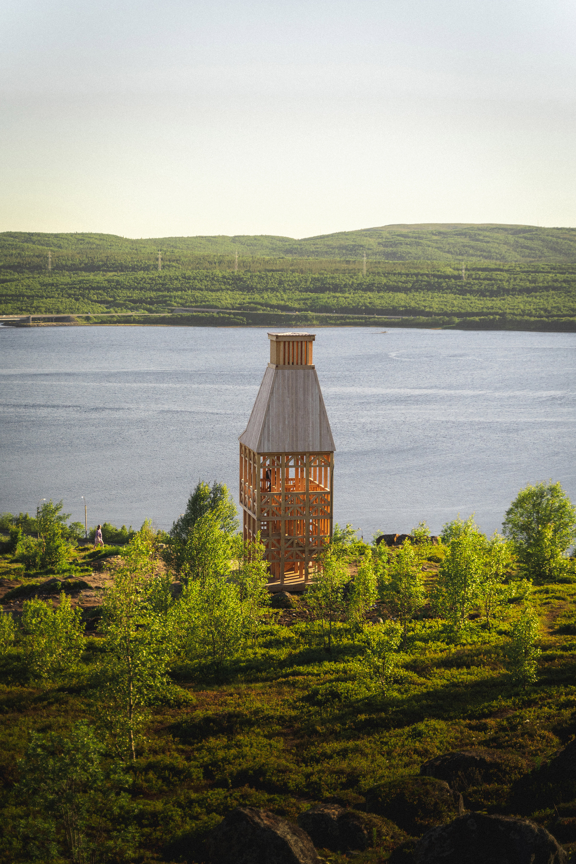 Timber observation tower with open slatted walls overlooking a lake and forested hills
