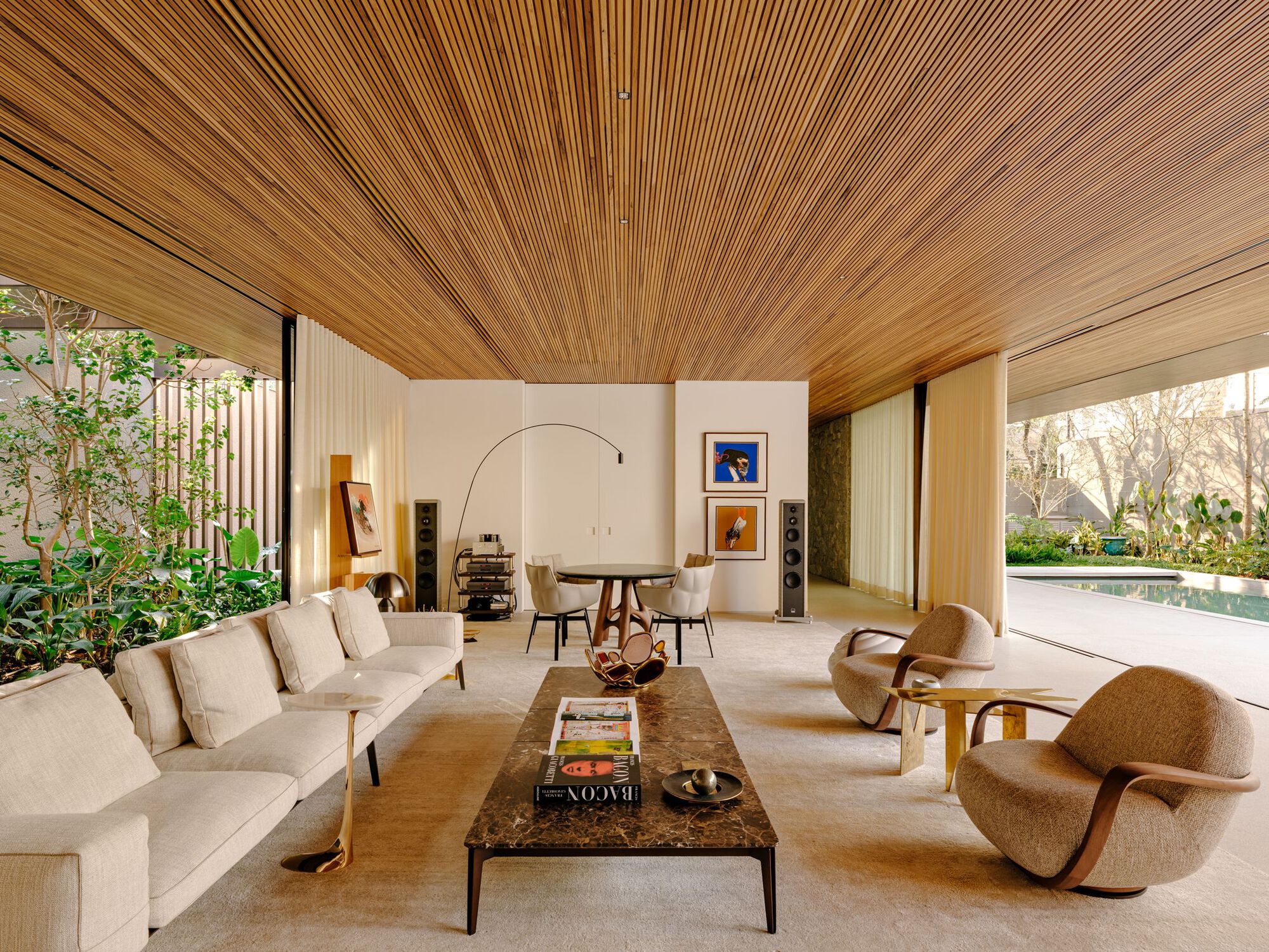 Living room with continuous timber slat ceiling and floor-to-ceiling glass opening to planted courtyard and pool
