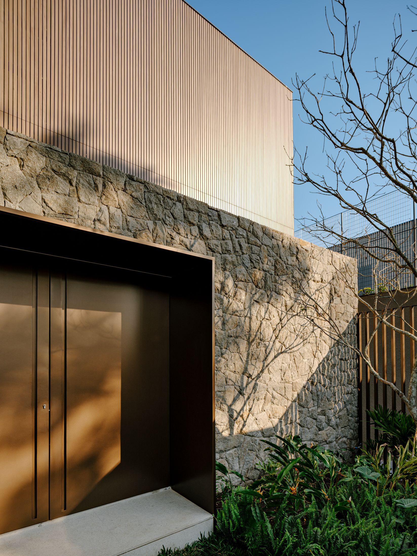 Bronze metal door entry set within stone wall beneath vertical timber facade