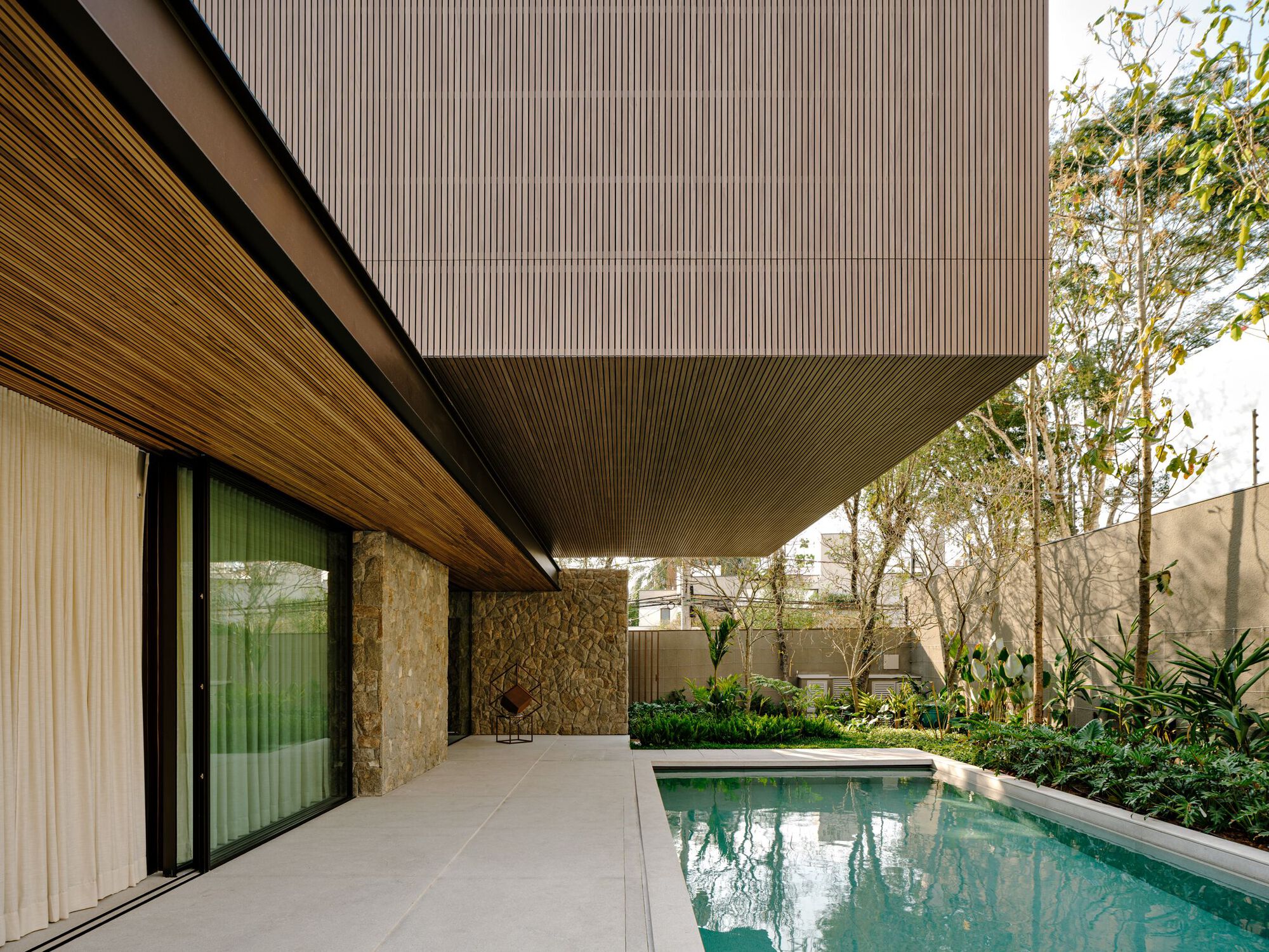 Poolside terrace with slatted timber soffit overhang and stone boundary wall