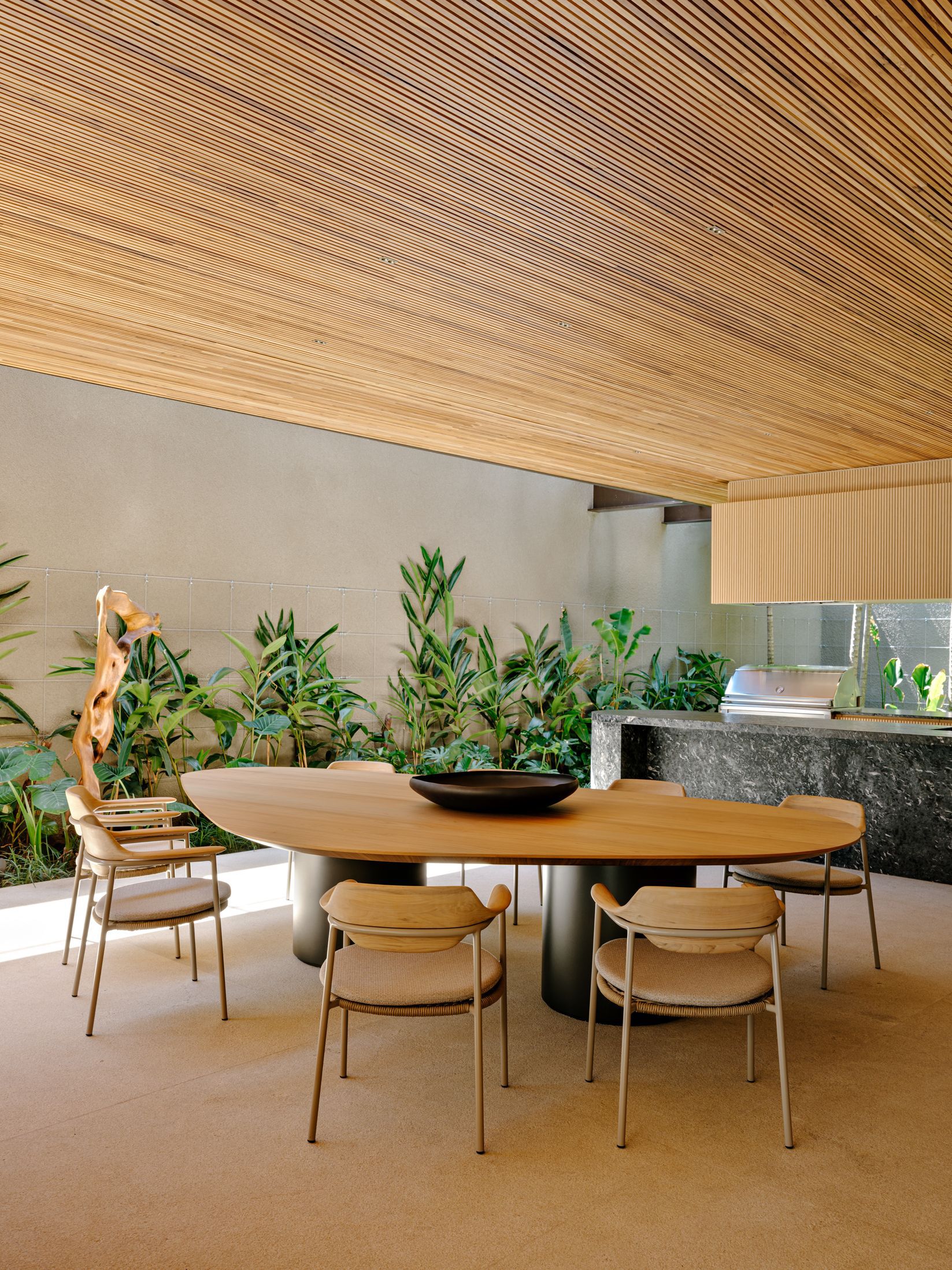Dining area with timber slat ceiling above an oval table and planted bed along the wall