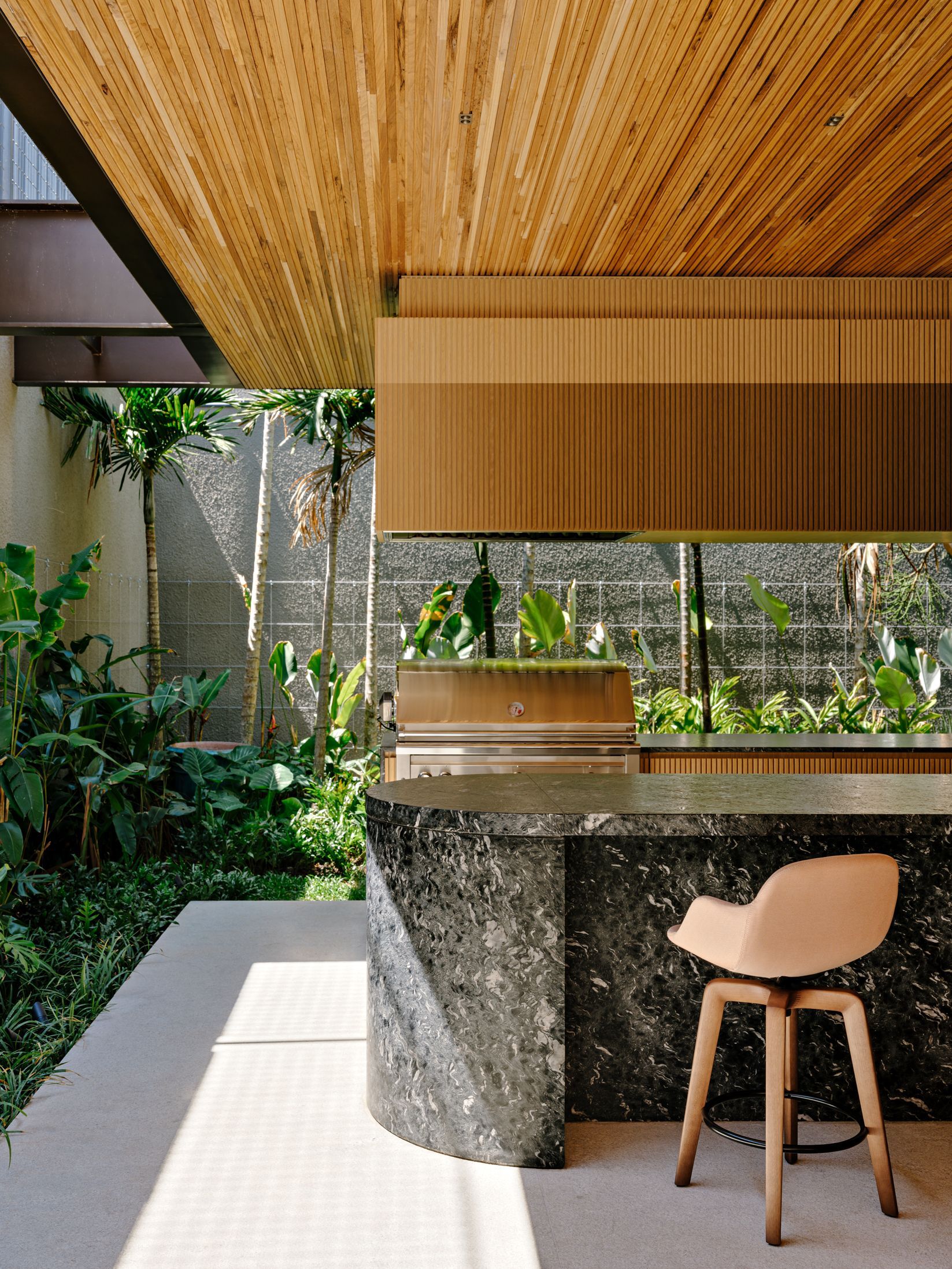 Outdoor kitchen counter with dark stone base and timber hood opening to a planted courtyard