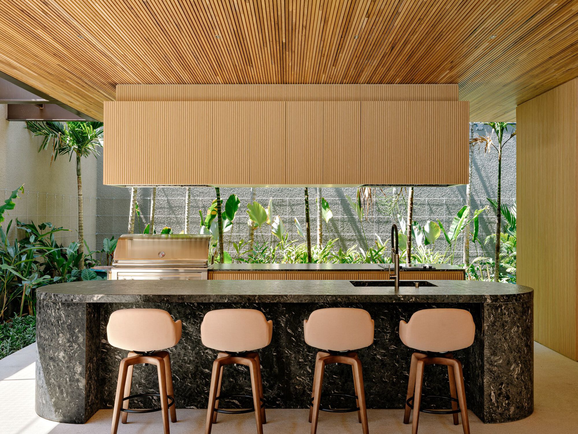 Kitchen island with charcoal stone facing and four bar stools beneath a timber slat ceiling