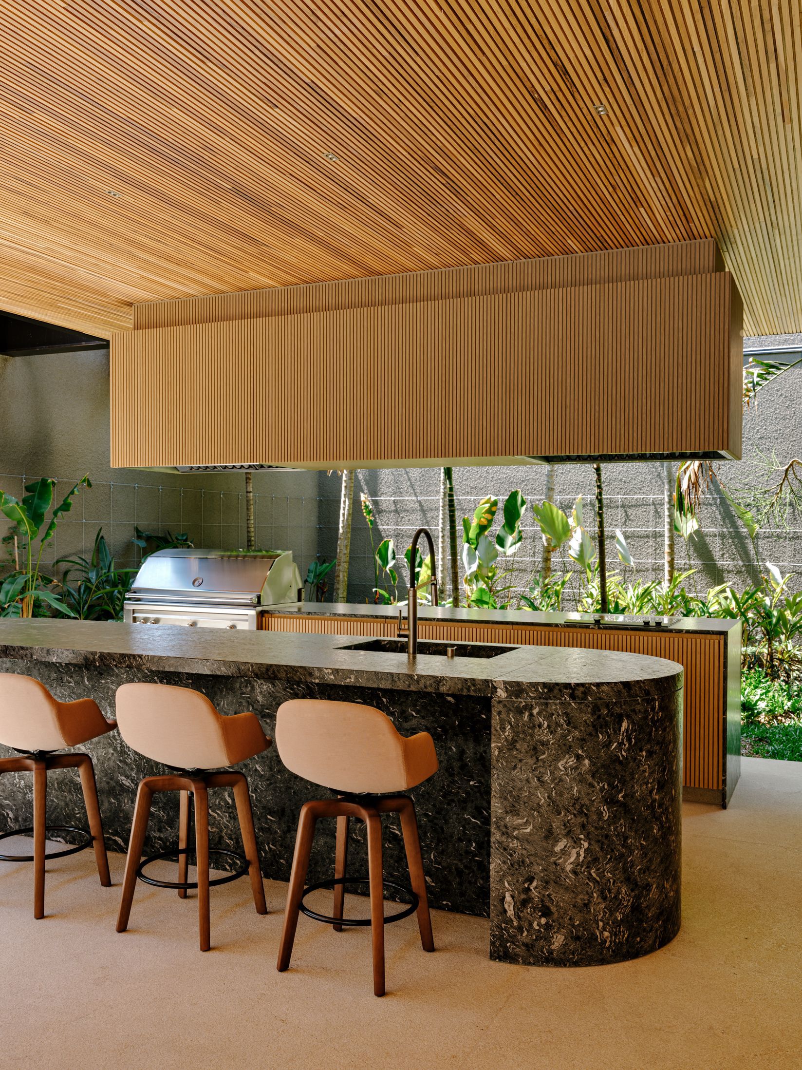 Curved kitchen counter with embedded grill and terrazzo stone cladding overlooking planted garden beds