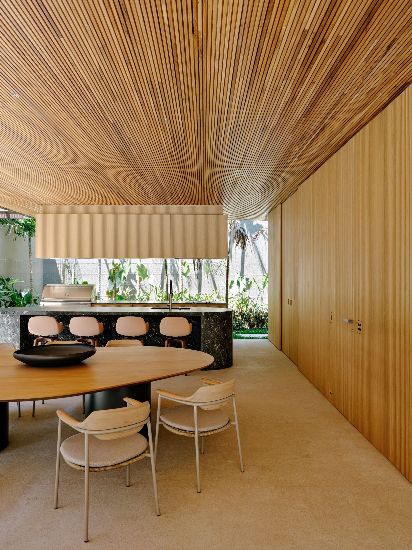 Open kitchen and dining area under continuous slatted timber ceiling with planted courtyard visible through clerestory window