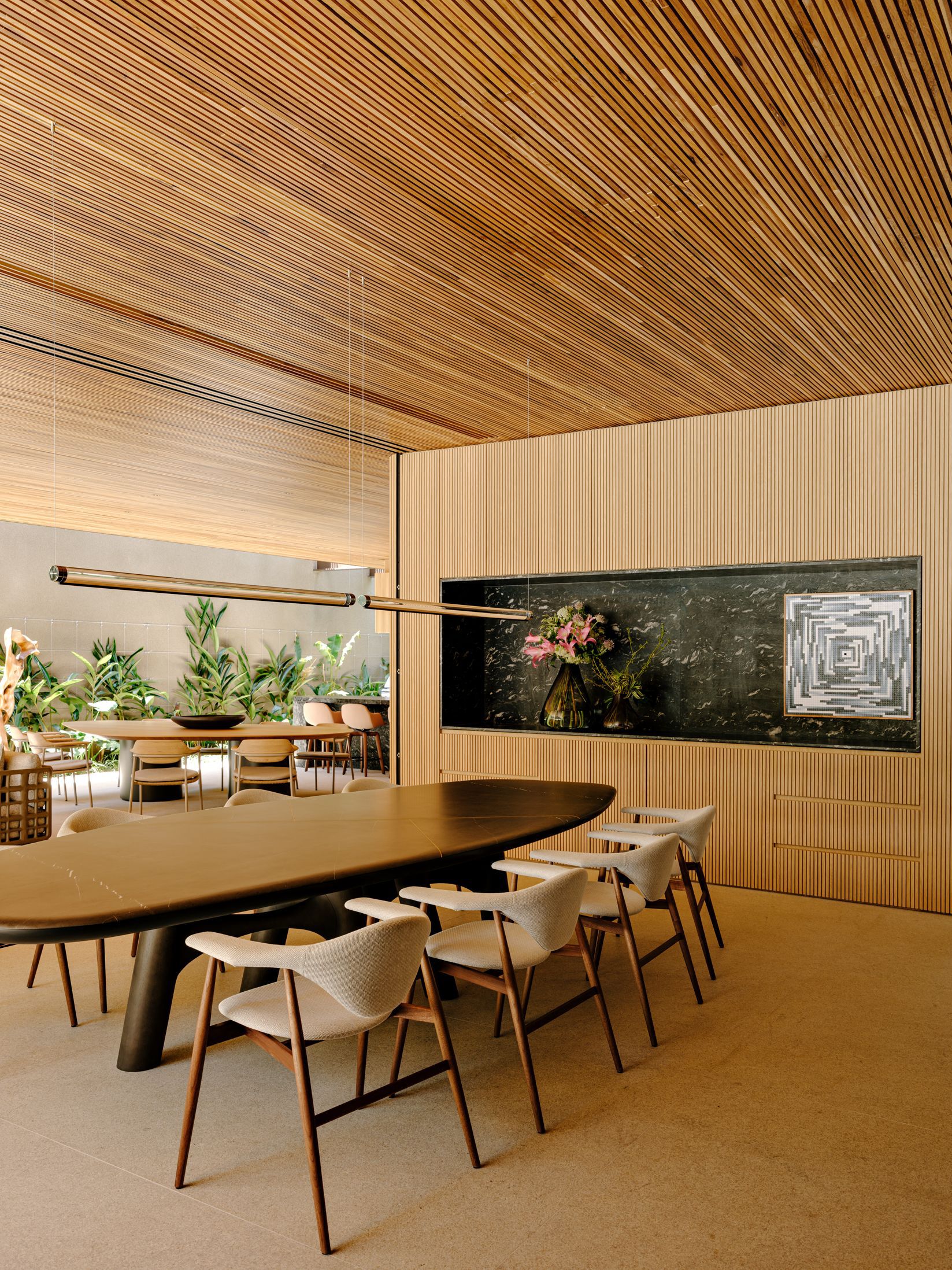 Dining room with long table beneath folded timber slat ceiling and dark marble panel set into ribbed wood cabinetry