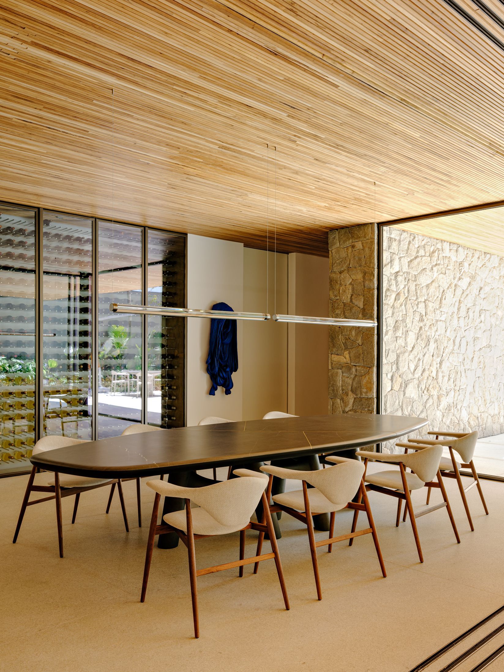 Dining area framed by textured stone wall and continuous ribbed timber ceiling with glazed courtyard views beyond