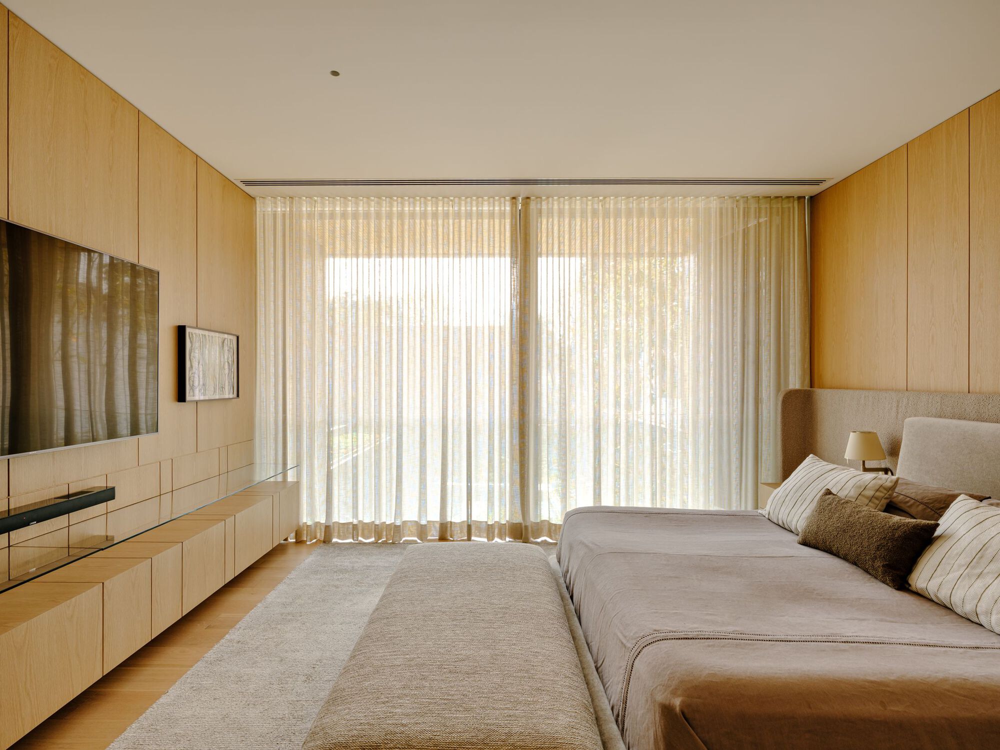 Bedroom with floor-to-ceiling sheer curtains filtering soft daylight and timber millwork built into the walls
