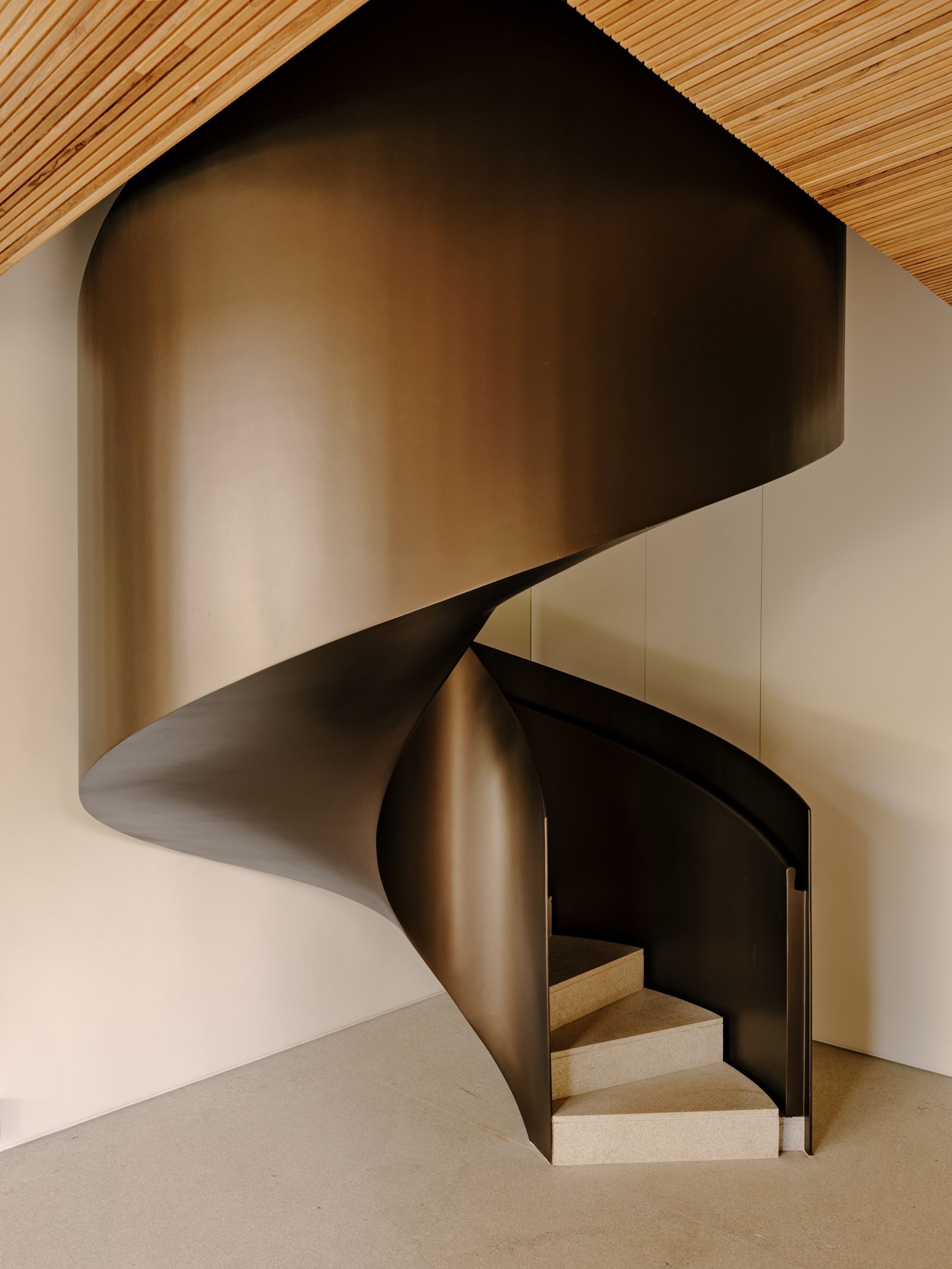 Sculptural bronze spiral staircase with folded metal balustrade beneath a ribbed timber ceiling