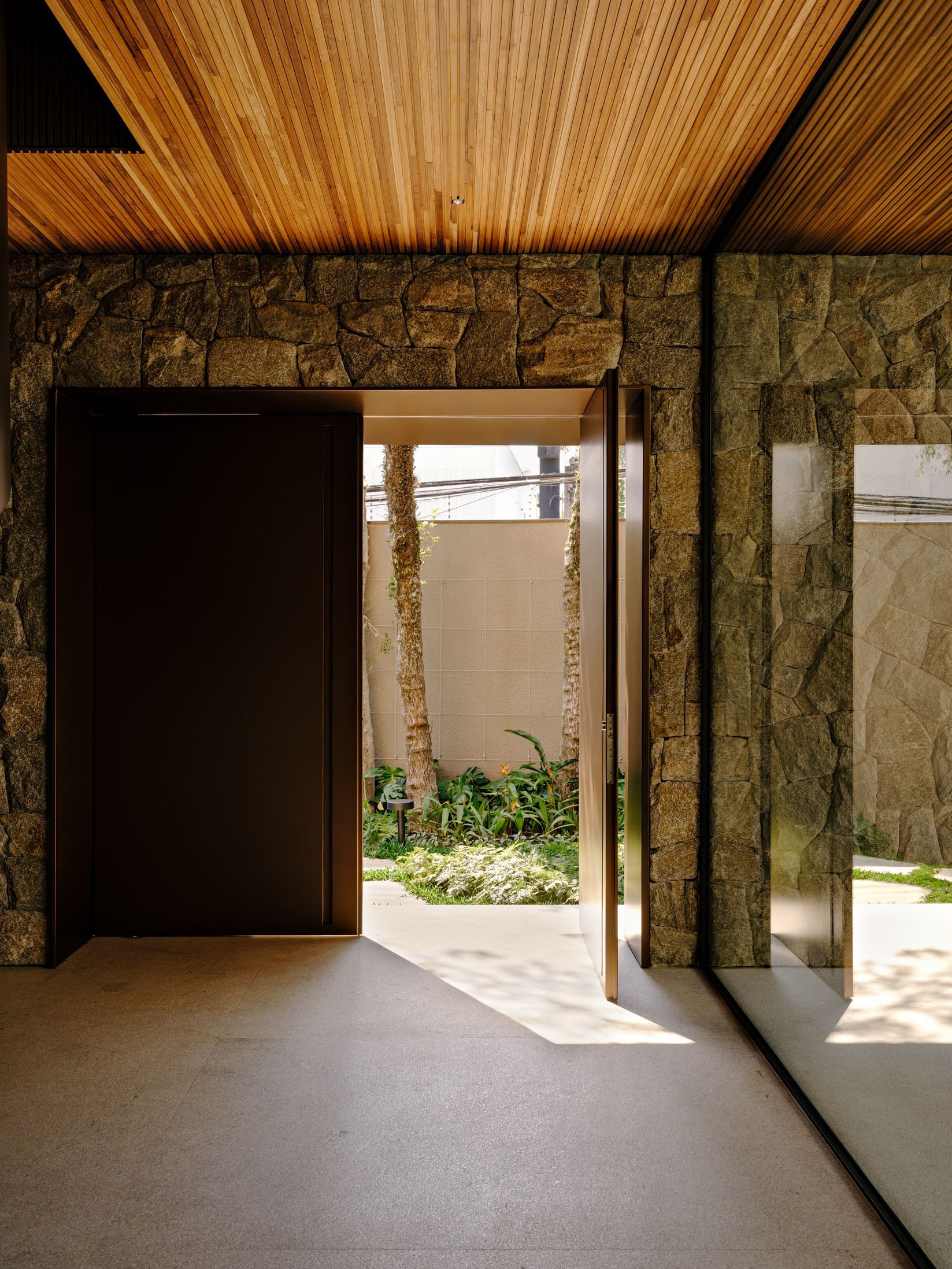 Entrance foyer with slatted timber ceiling and rough stone wall opening to a planted courtyard