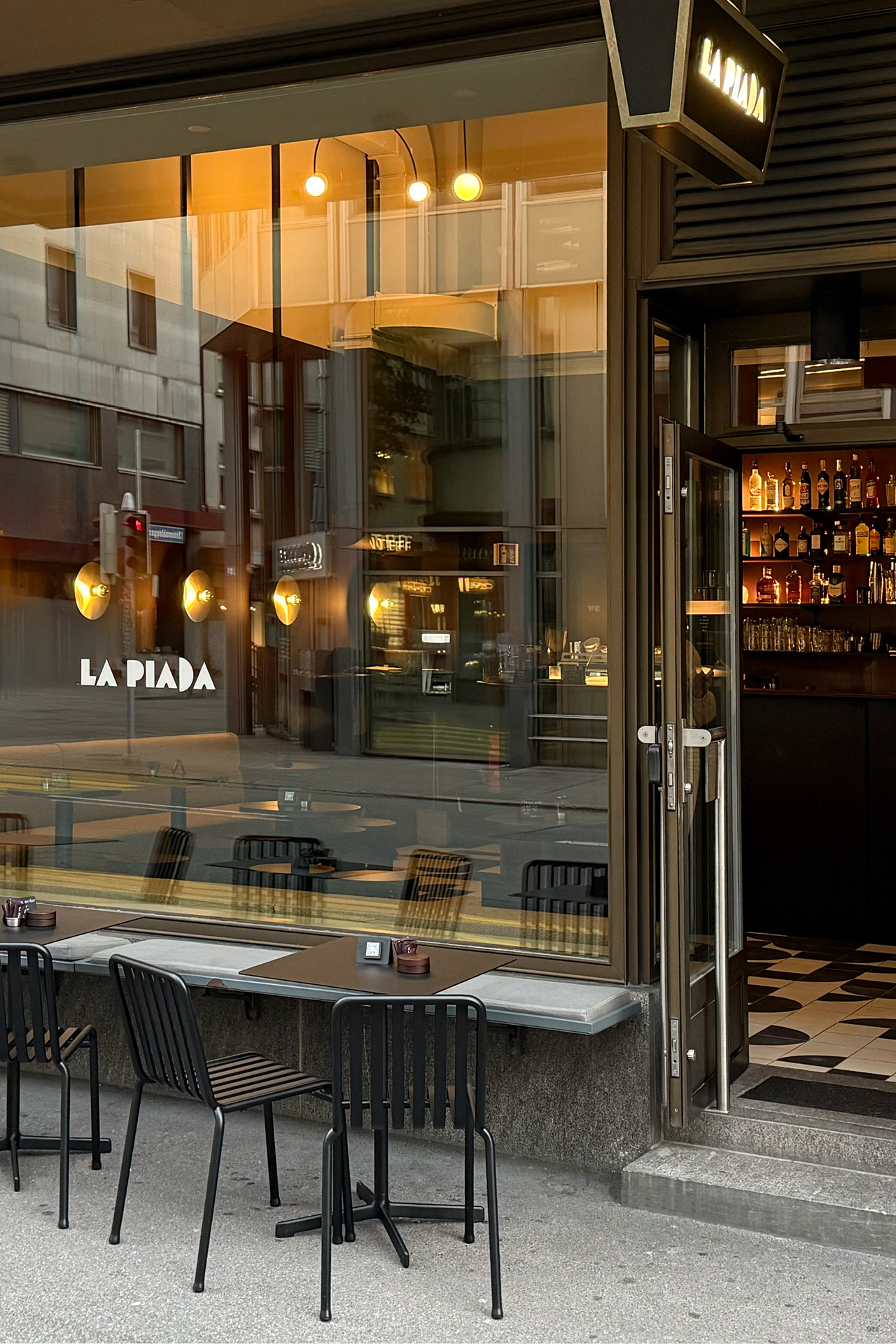 Street-facing glazed facade with open door revealing interior bar at dusk