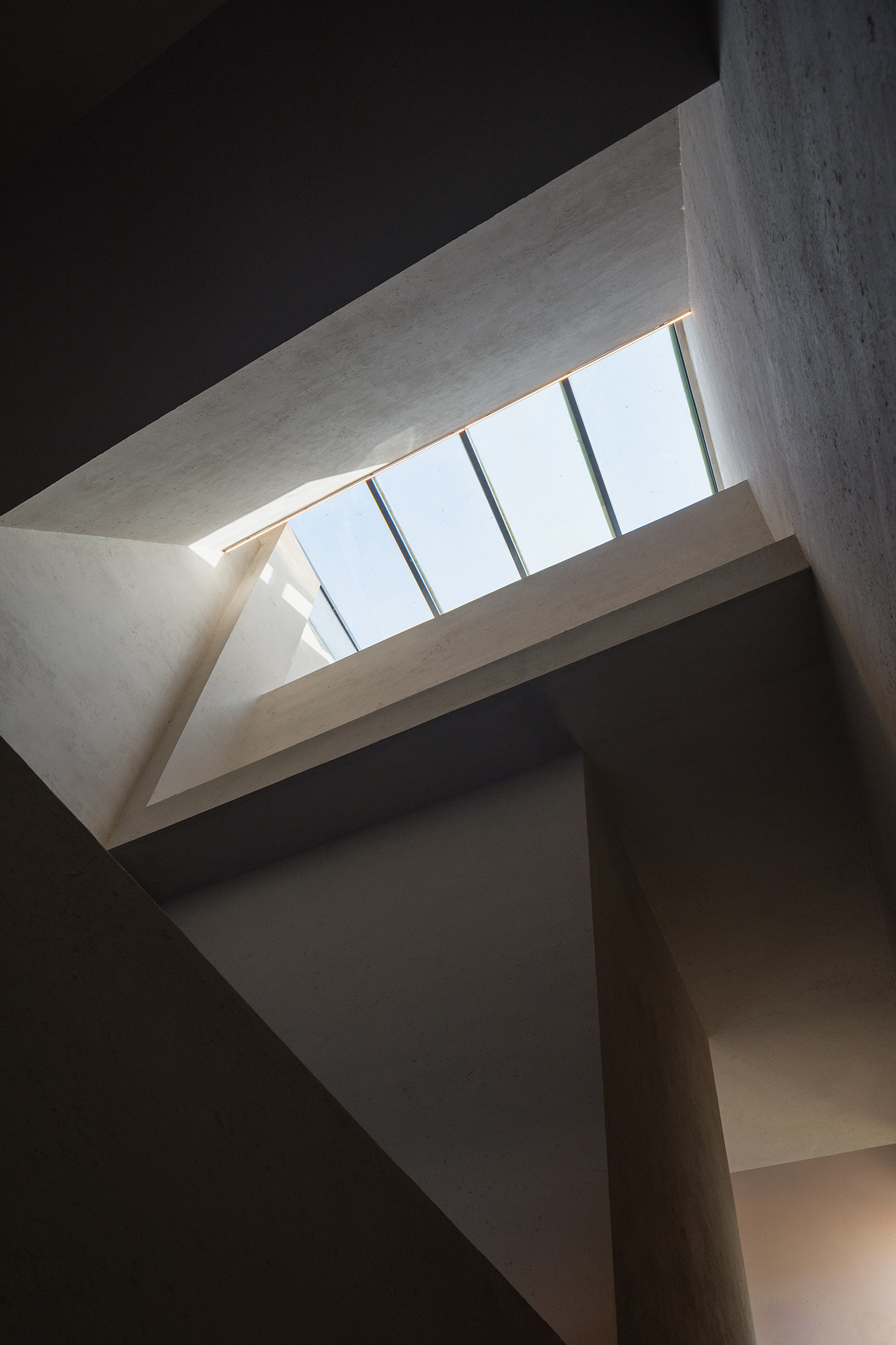 Interior skylight view showing angled concrete beams framing a row of clerestory glazing against sky