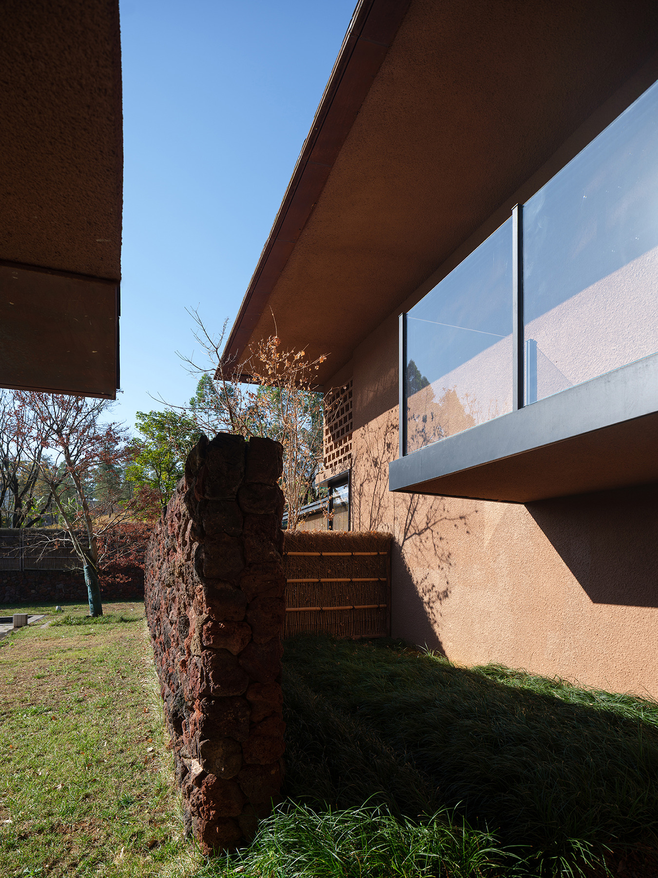 Cantilevered terrace soffit and red volcanic stone wall beneath glass balustrade in morning light