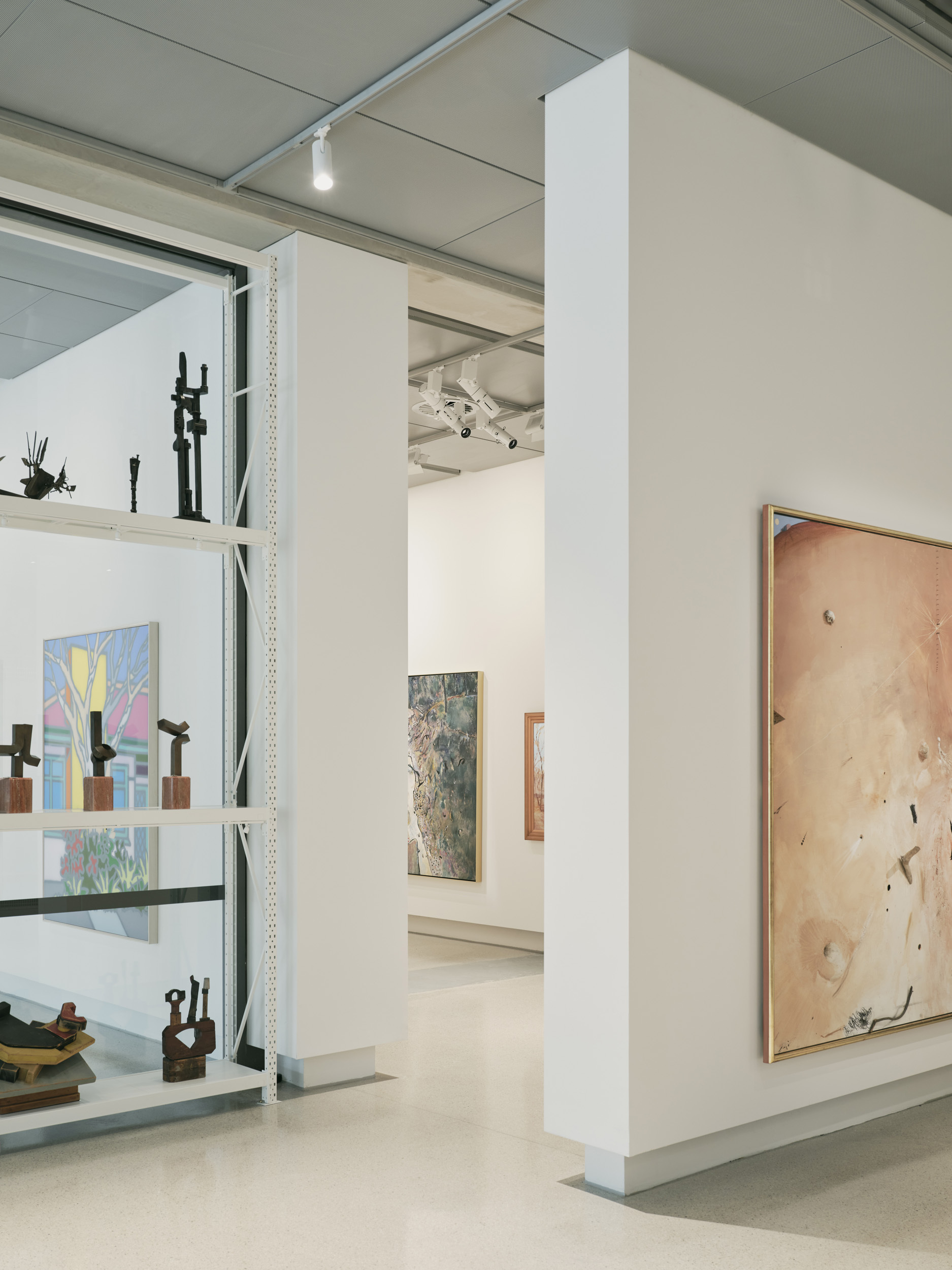Gallery interior with white partition walls displaying artworks on metal shelving and hung on plywood panels