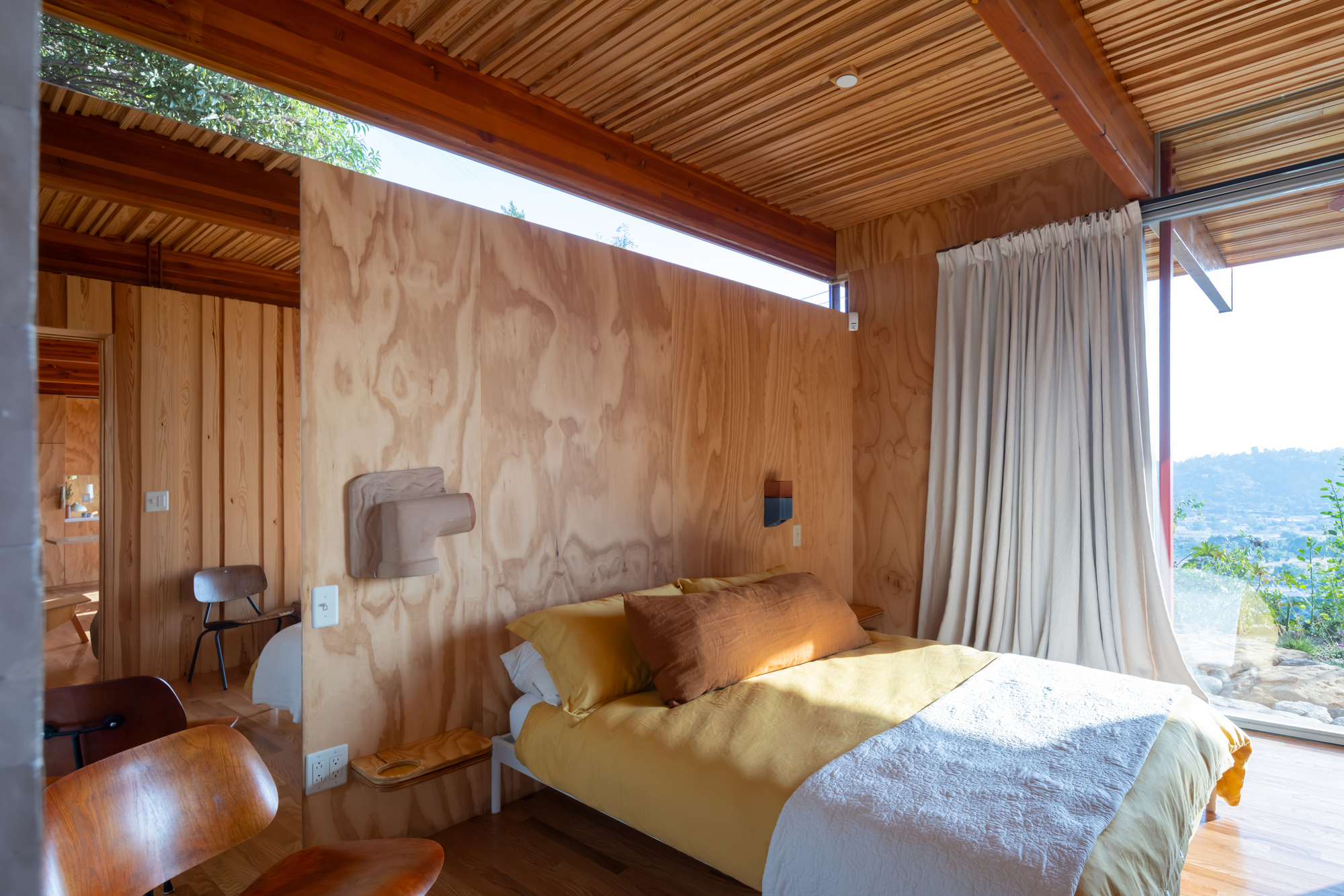 Bedroom with plywood headboard wall and clerestory window casting natural light onto the bed