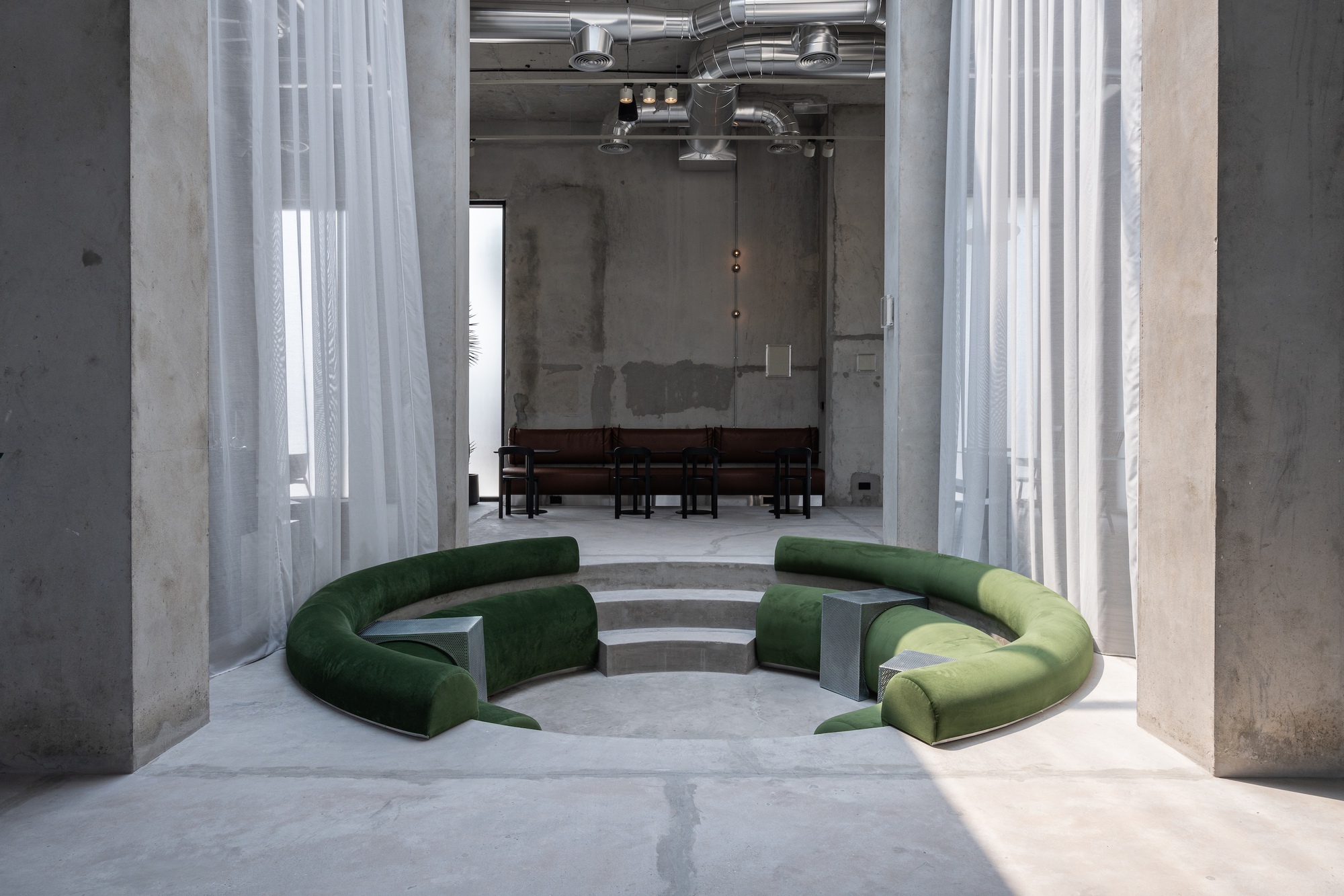 Sunken circular seating pit with green upholstered benches between white sheer curtains