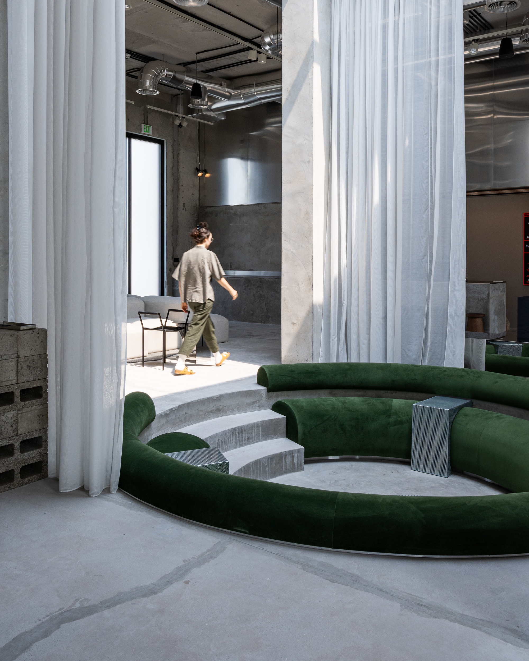 Figure walking past stepped concrete seating and white fabric partitions in afternoon light