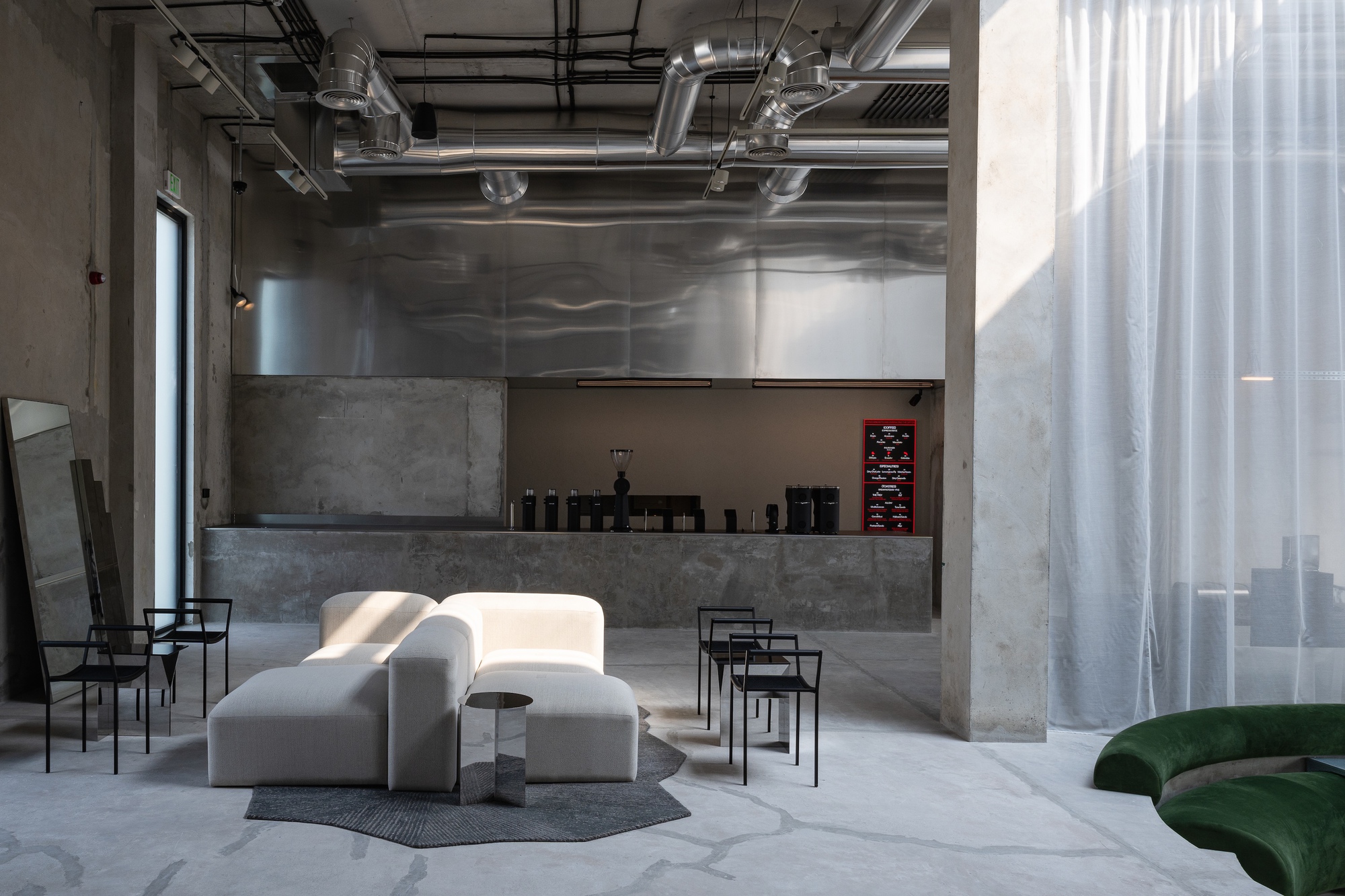 Polished concrete counter and steel hood under exposed ductwork and ceiling infrastructure with sunlight streaming through curtains